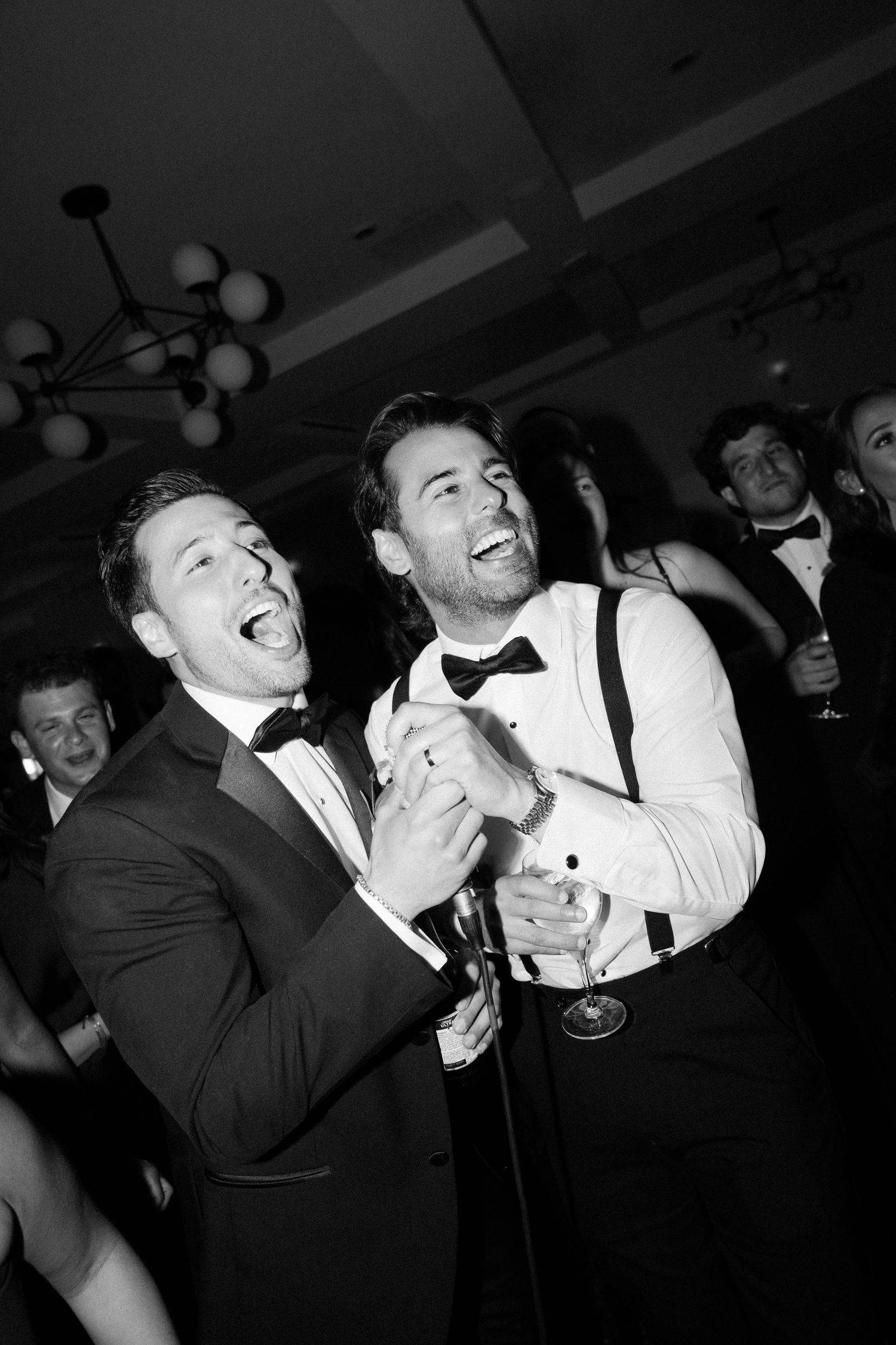 Guests celebrating and having fun at a lively black tie event with drinks in hand.
