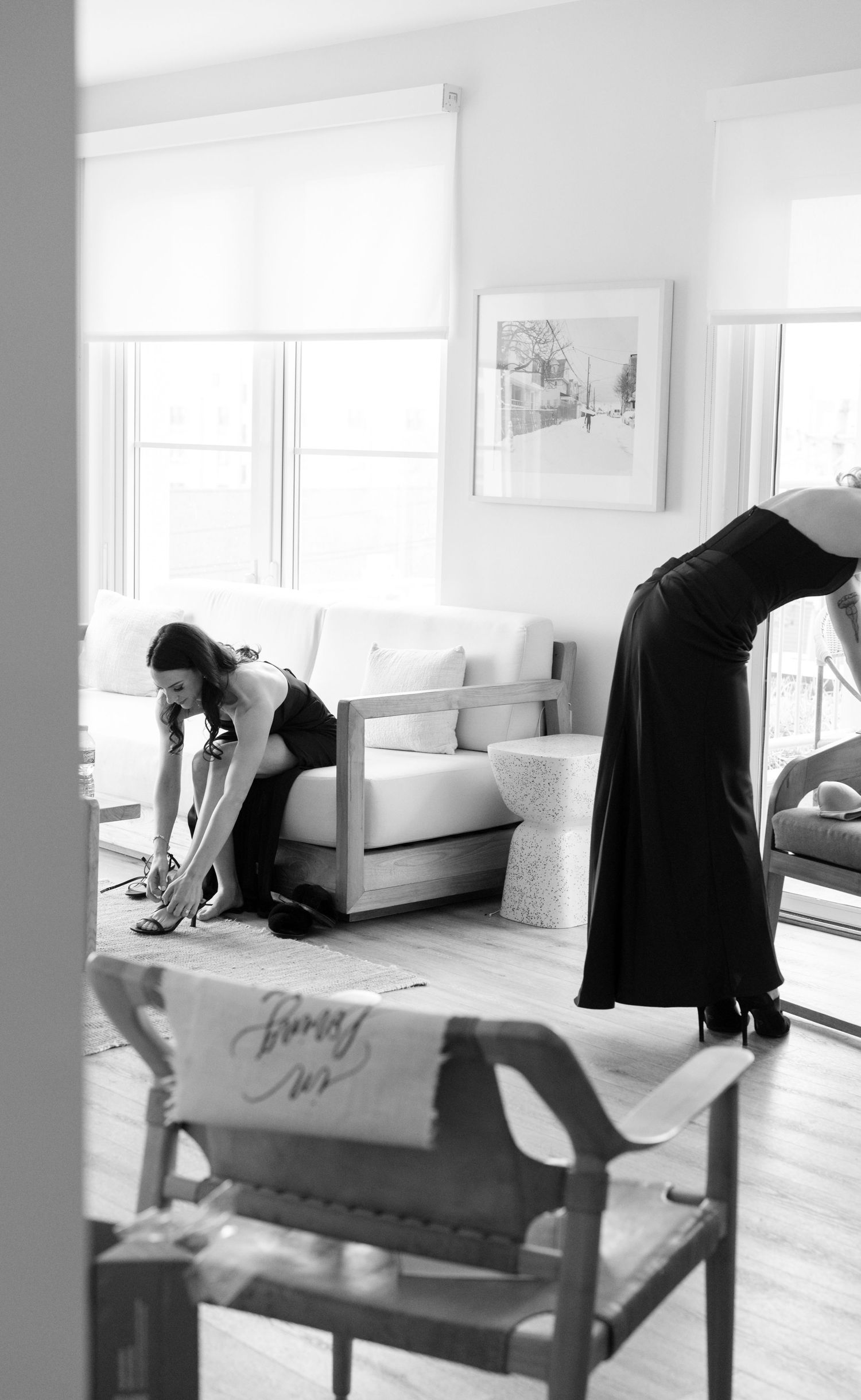 Black and white photo of two people stretching or exercising in a bright minimalist room with white walls and windows.