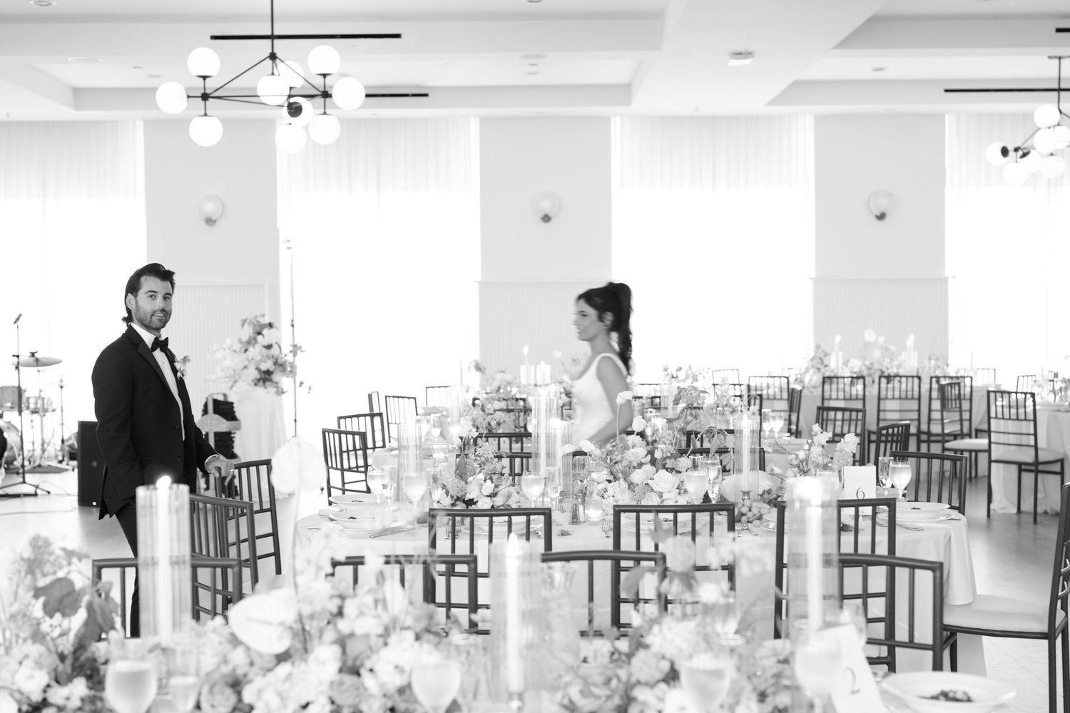 Empty wedding reception venue with tables and chairs set up in a bright white room.