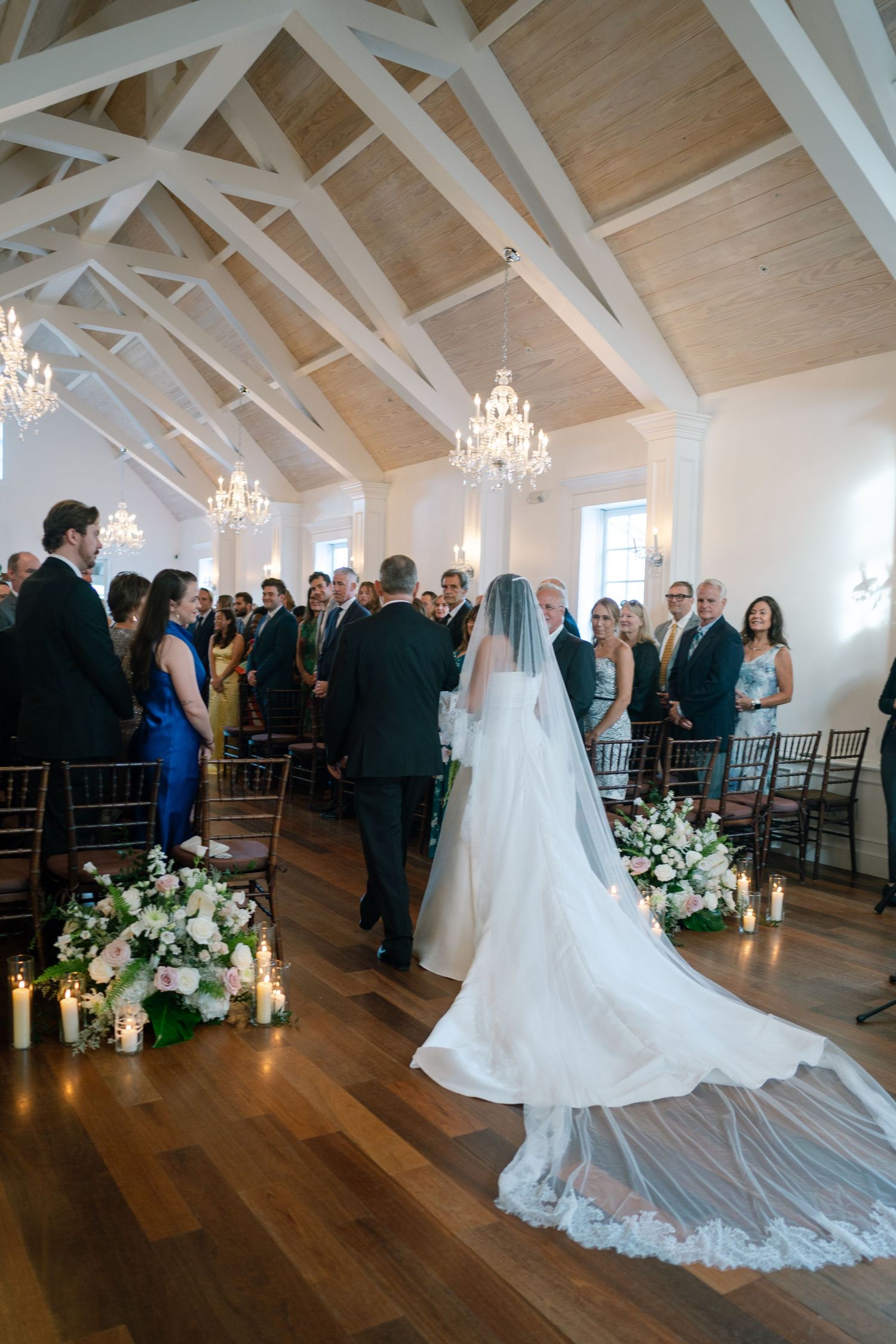 A cathedral-length veil trails behind a bride in a stunning white gown during a wedding ceremony.
