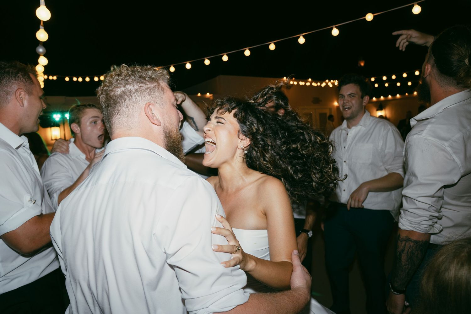 Wedding reception celebration with string lights and dancing under the night sky.