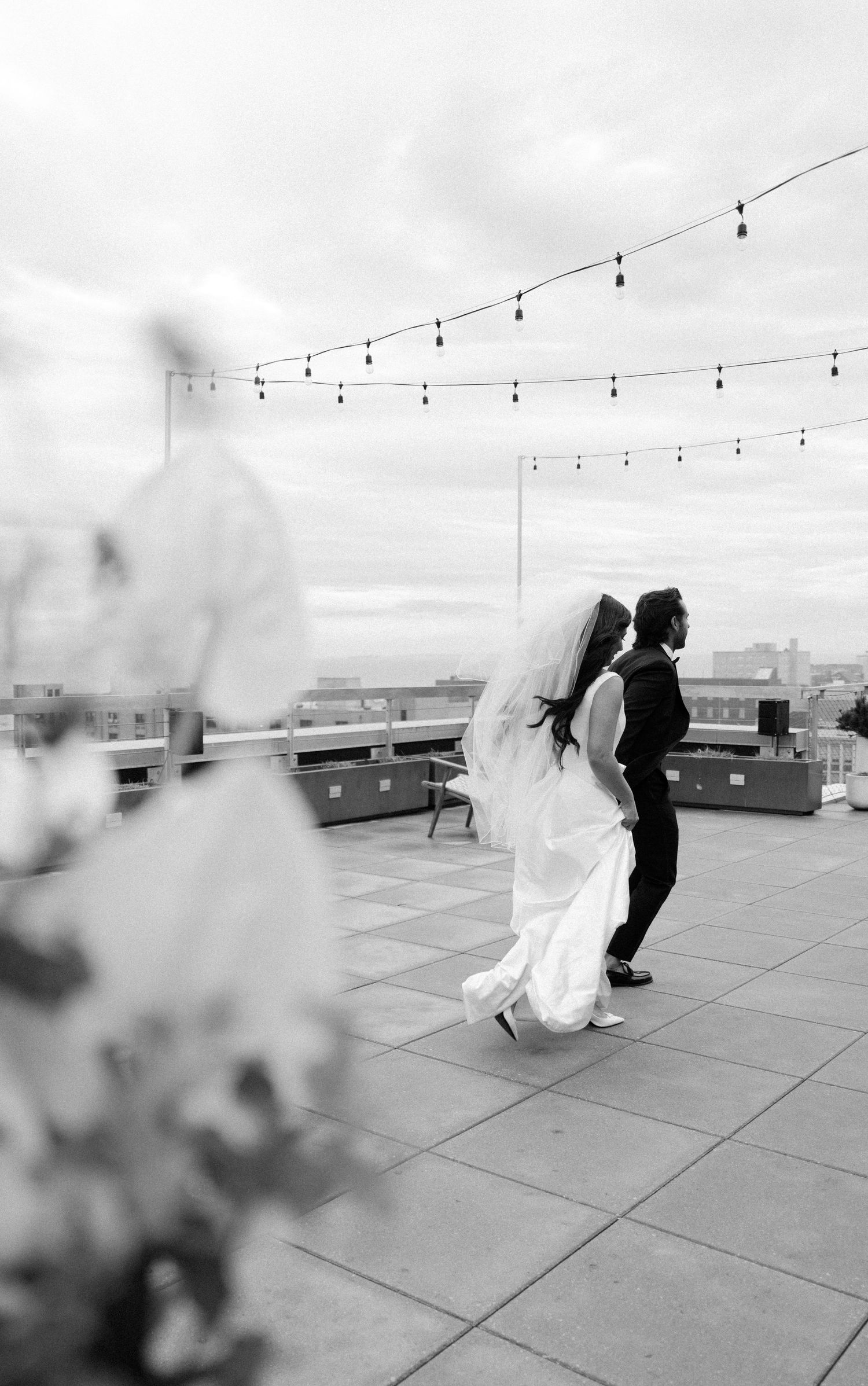 A couple dances on a rooftop venue with string lights overhead in black and white photography.