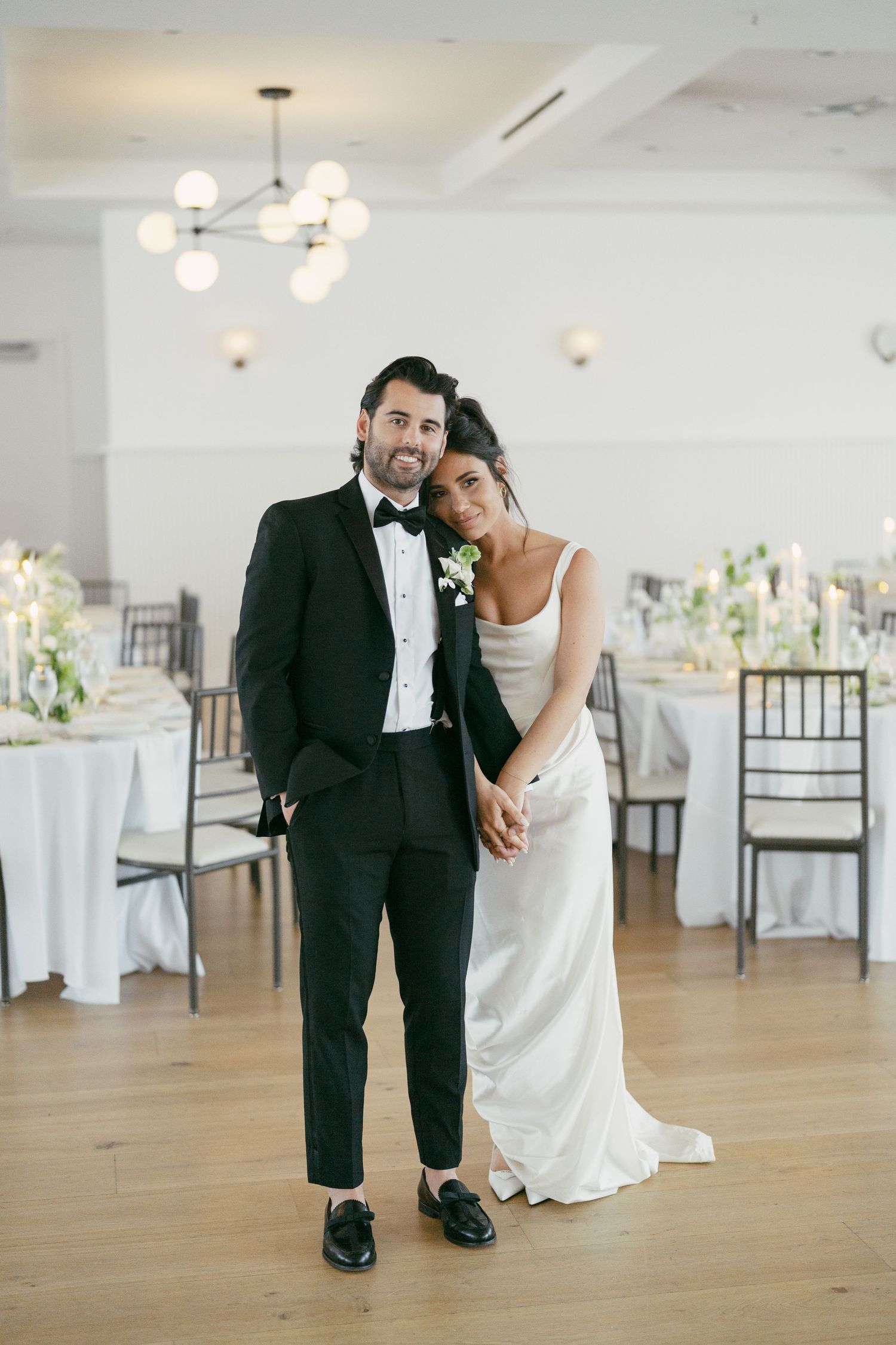 Elegant wedding couple shares intimate moments in a bright reception hall with wooden floors.