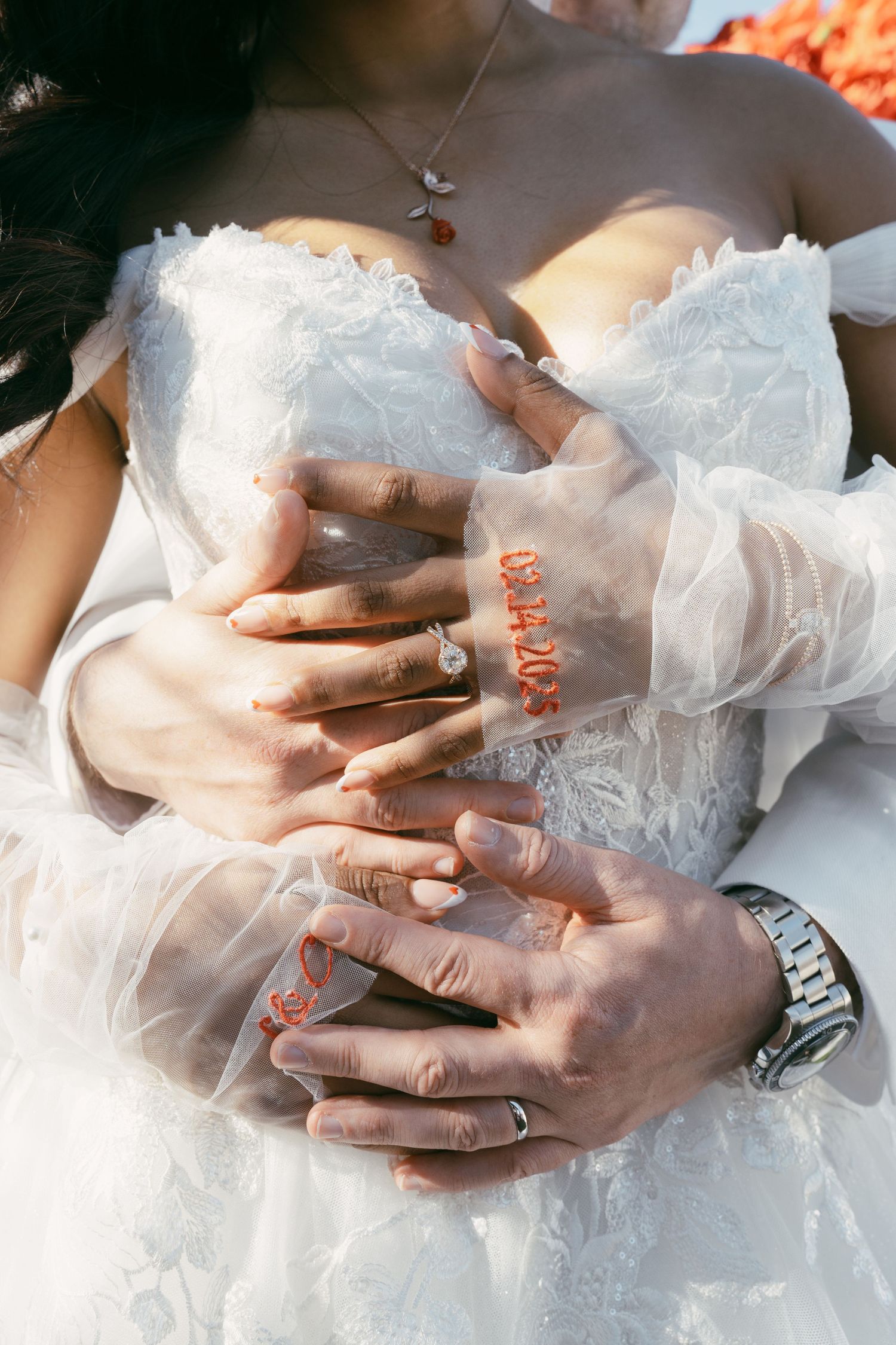 Close-up of hands with wedding rings resting on white lace dress.