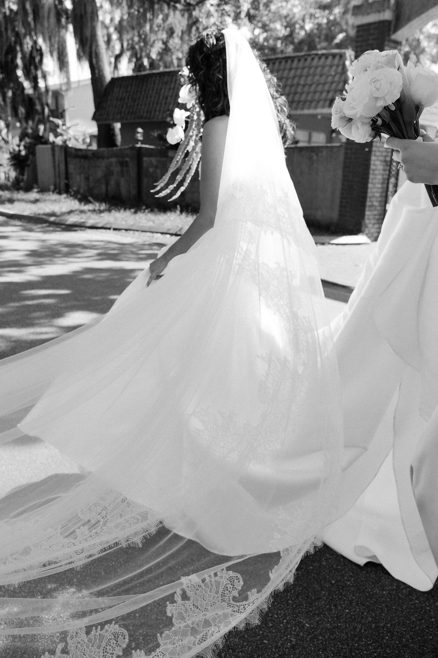 A flowing white wedding dress with a long lace train captured in black and white outdoors.