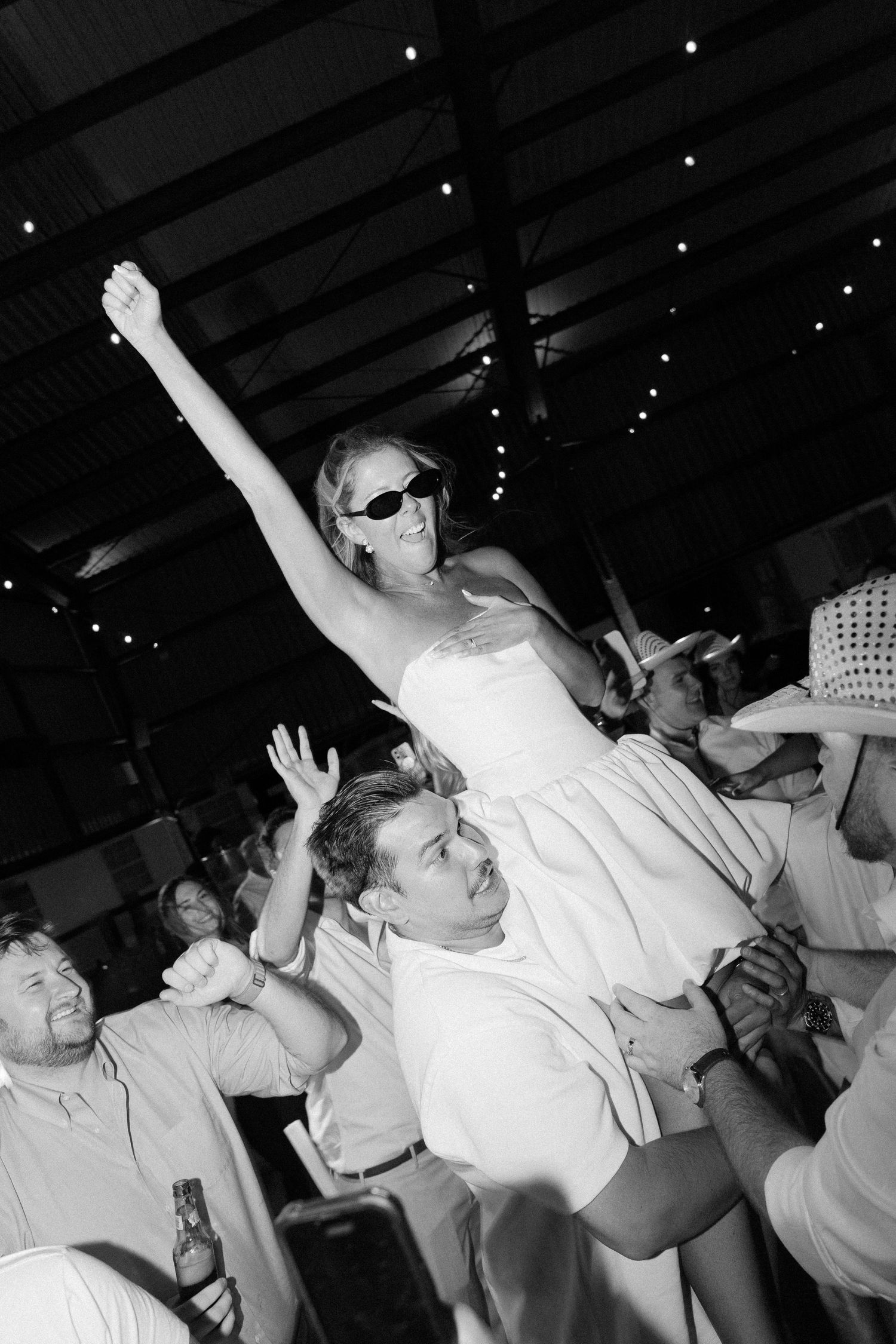A celebration scene with people dancing and one person being lifted up at a reception.