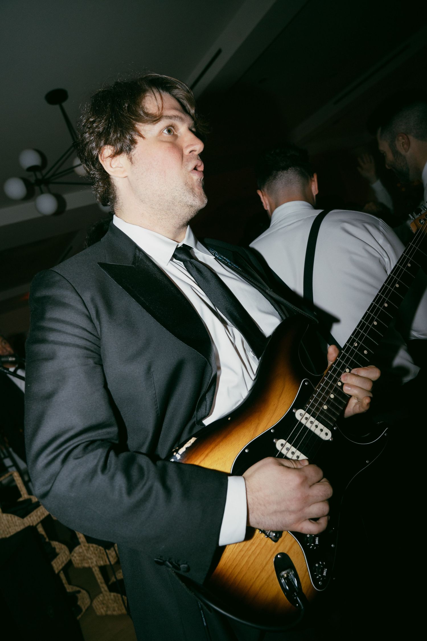 A musician in a dark suit plays an electric guitar during a live performance.