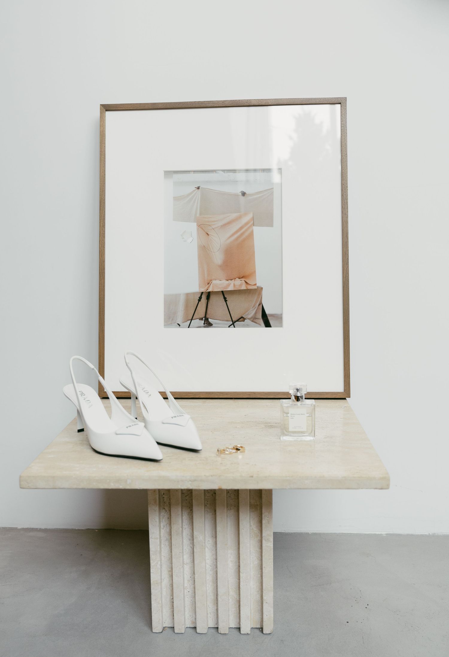 Minimalist white gallery space with travertine bench and framed artwork displayed on stark walls.