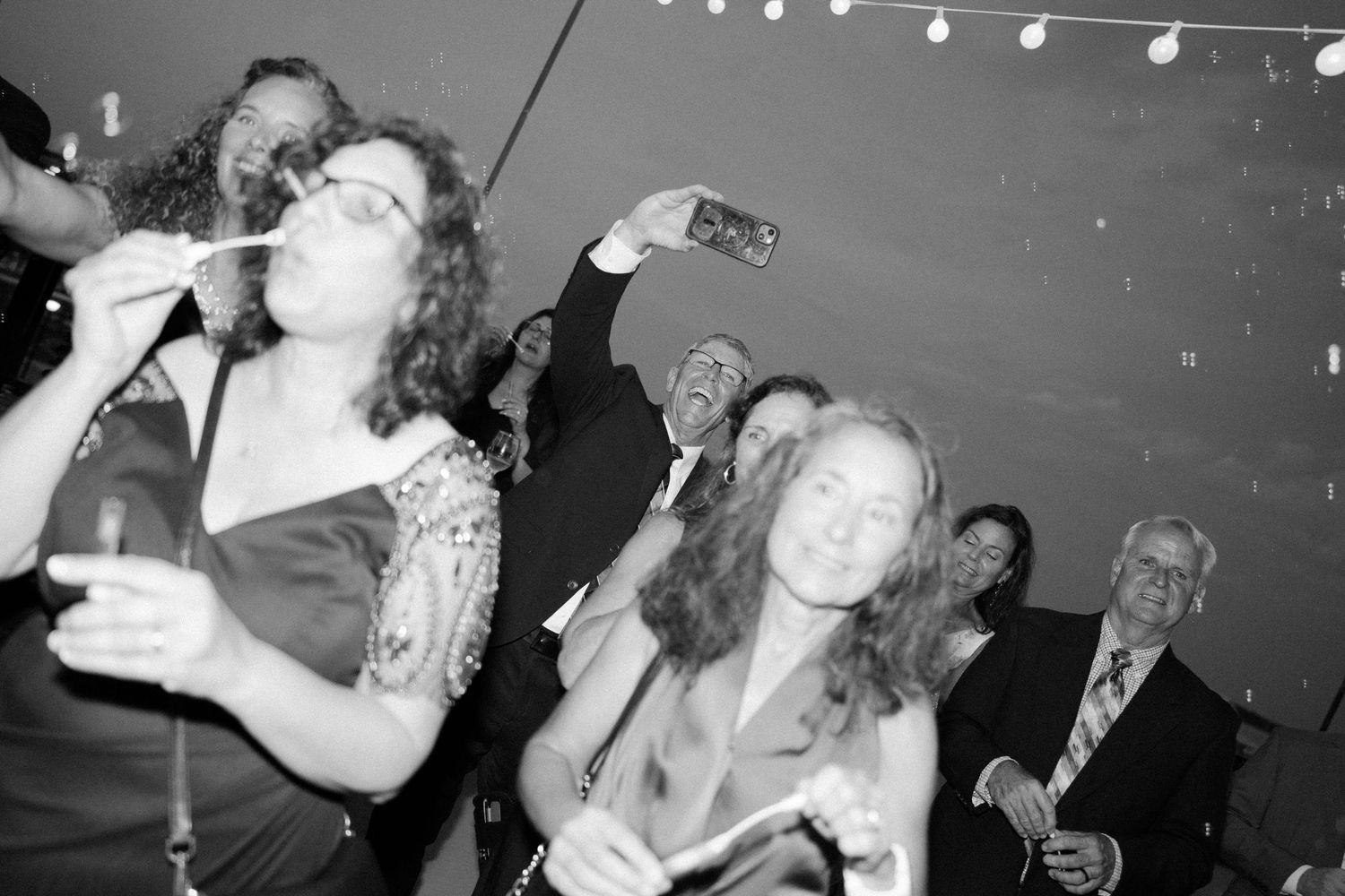 Black and white photo of wedding guests dancing and celebrating at reception.