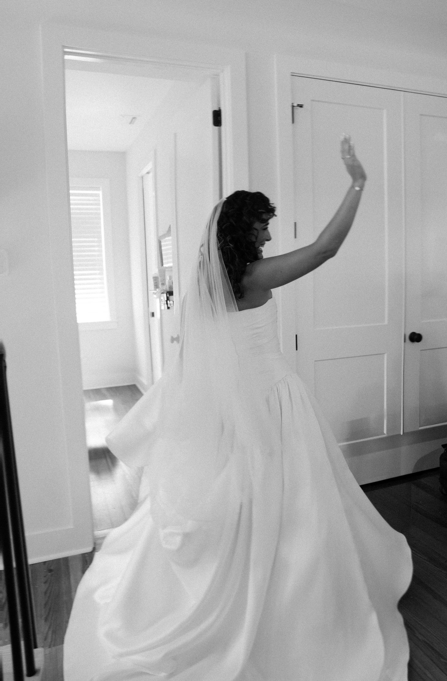 Black and white photo of a wedding dress with flowing train and veil in motion.