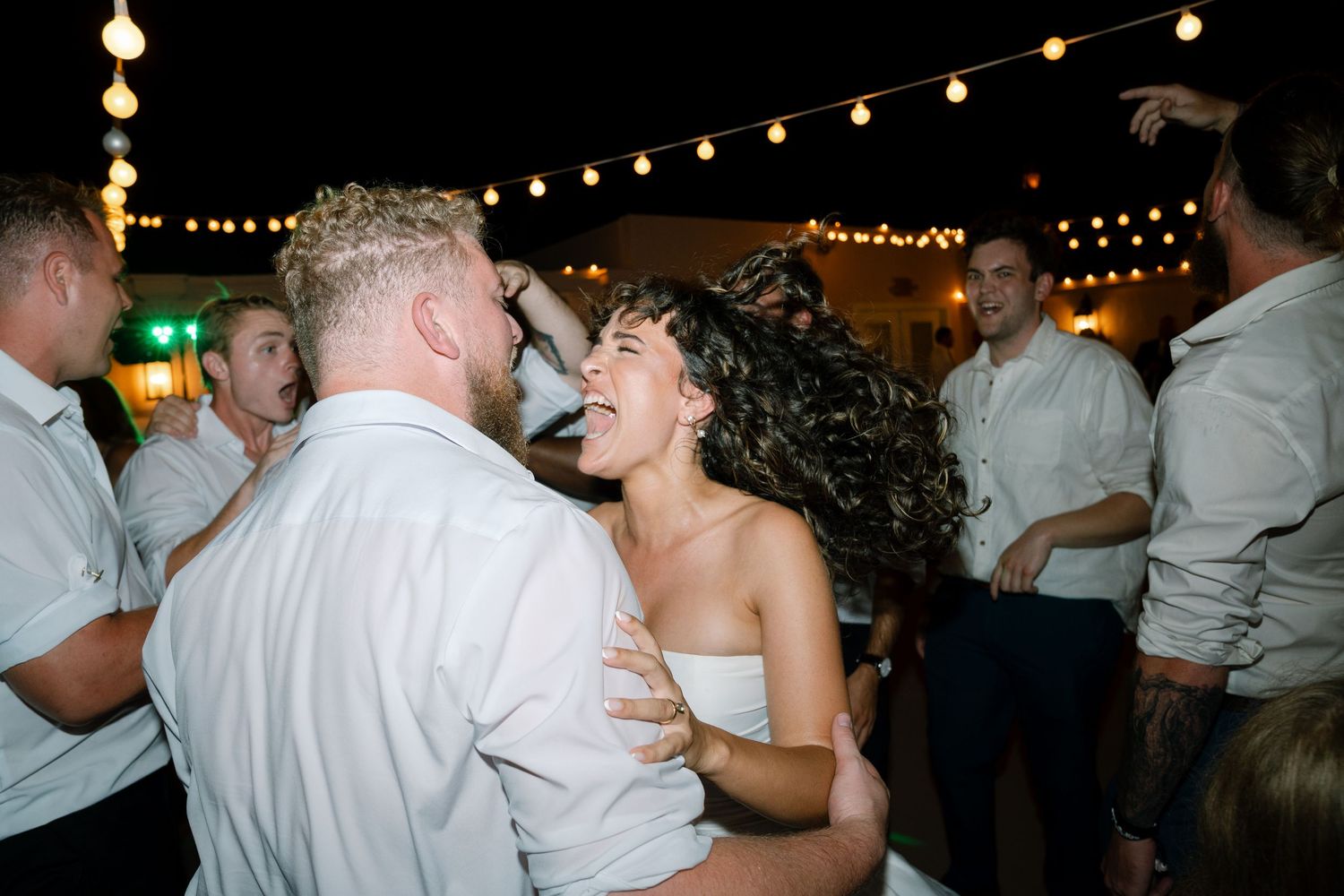A joyful dance moment captured under twinkling outdoor string lights at an evening wedding reception.