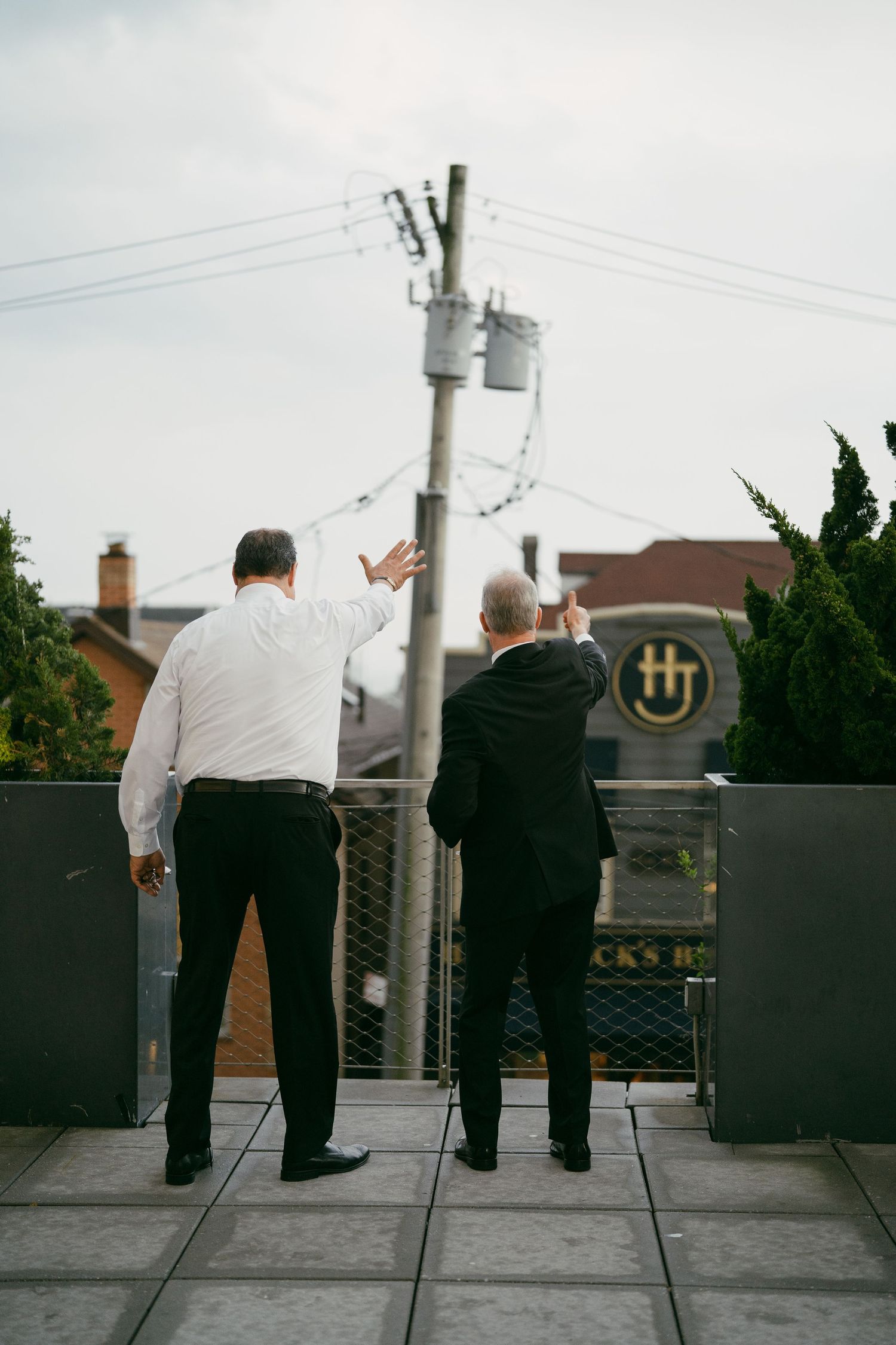 Wedding guests lean against rooftop railing while viewing cityscape at outdoor reception venue.