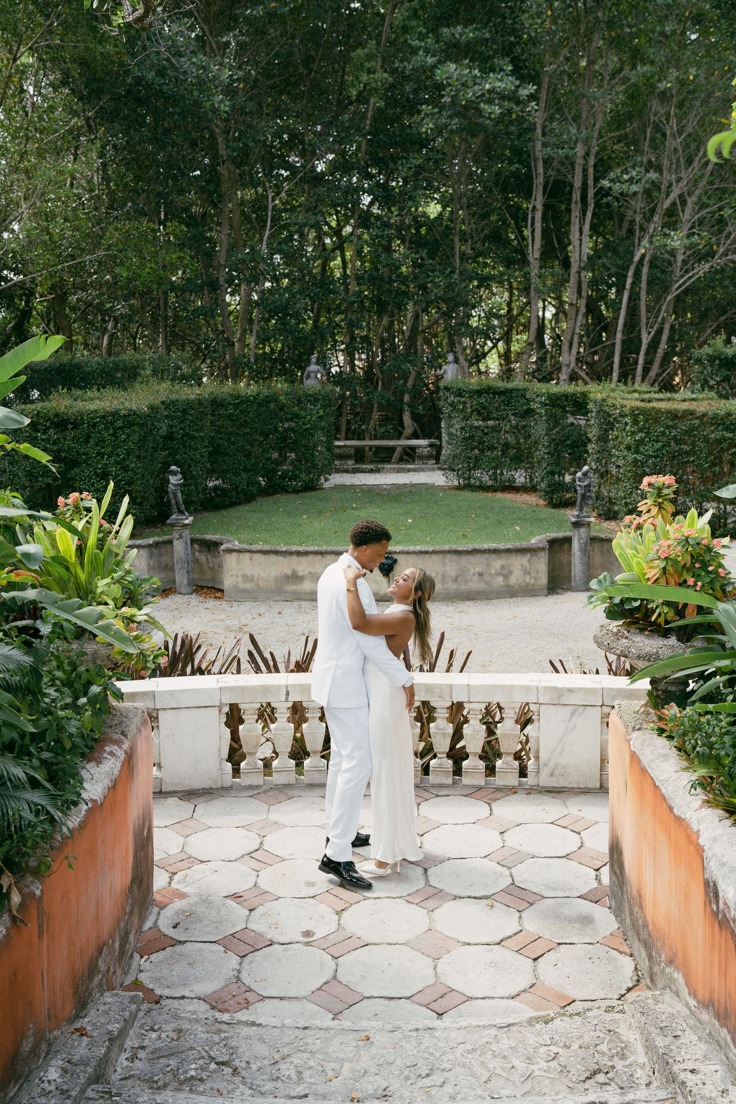 Romantic garden wedding portrait on stone terrace surrounded by lush greenery.
