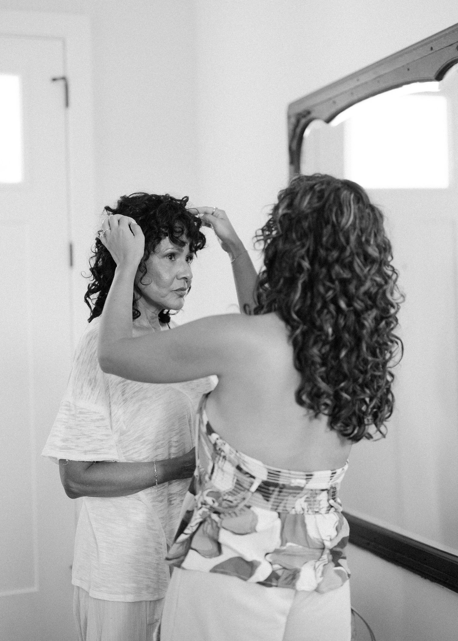 Black and white image of two women with curly hair getting ready in formal attire.