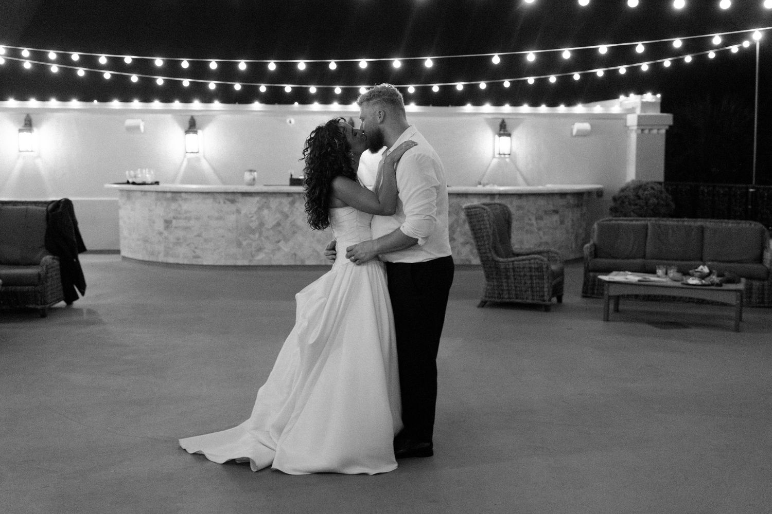 Couples dancing under romantic string lights at an outdoor evening wedding reception.