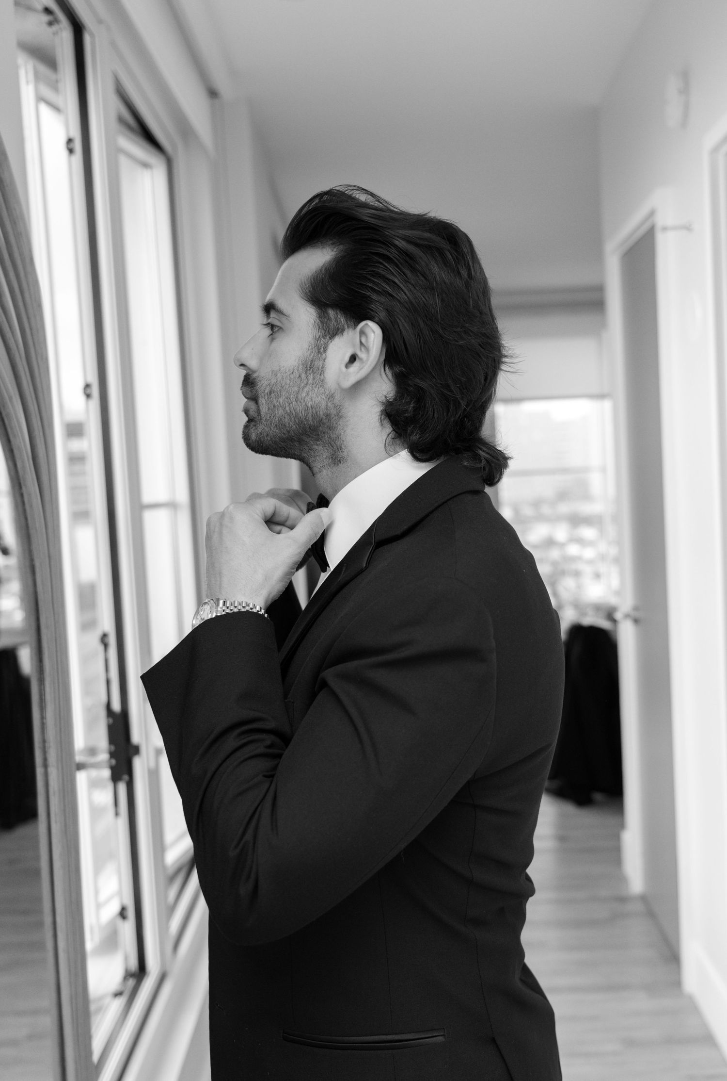 Series showing contemplative moments of groom in black suit by window in hallway.