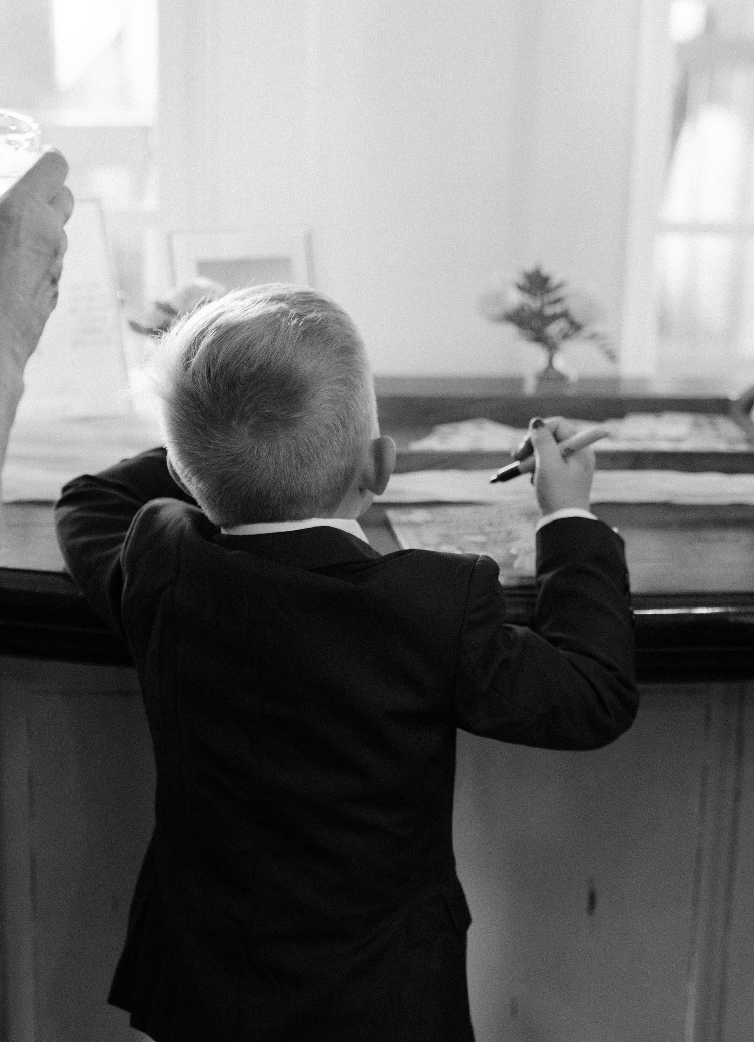 Young ring bearer in formal suit reaches up to counter in black and white photograph.