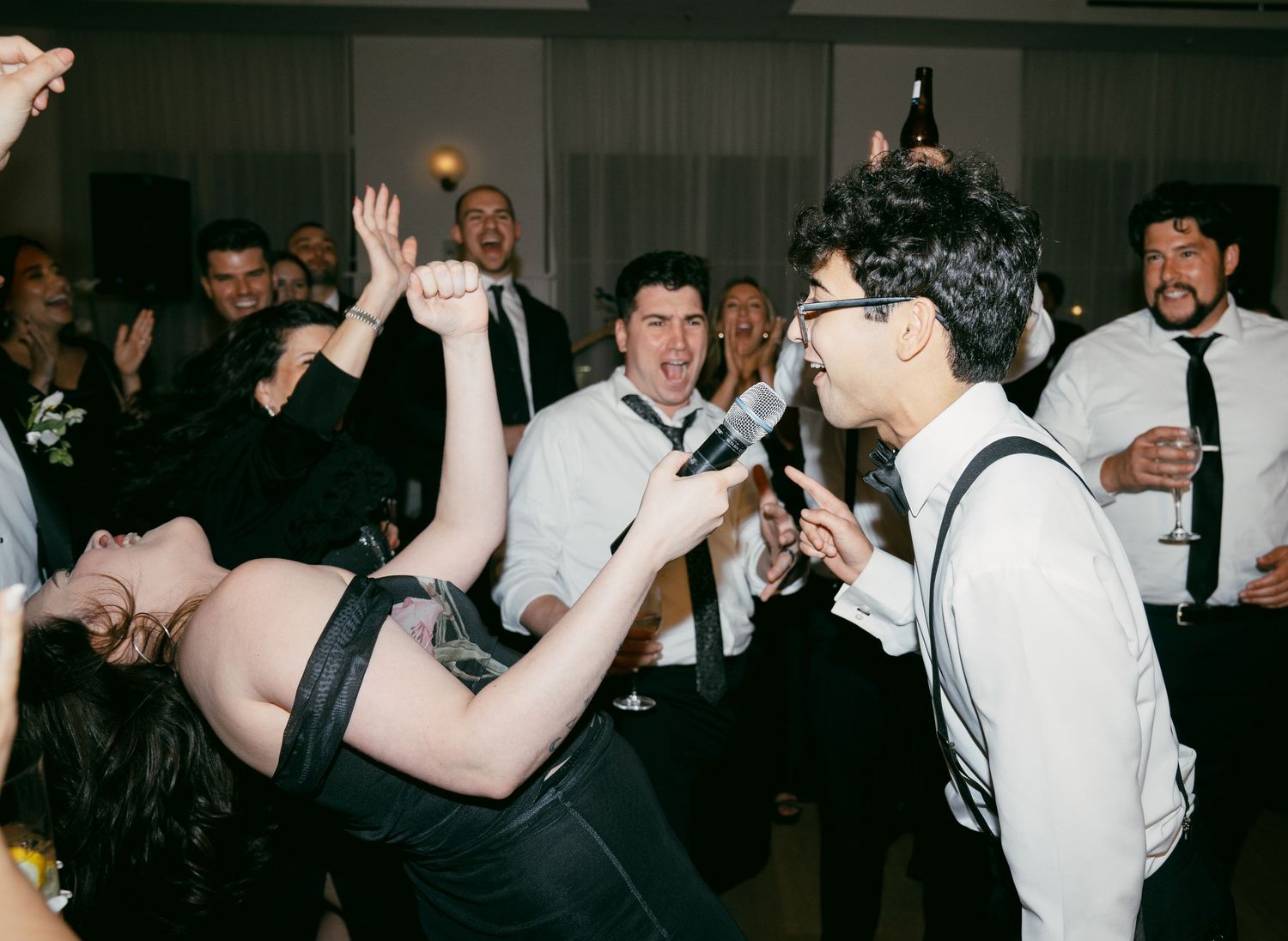 Wedding guests dance and sing enthusiastically at a lively reception party.