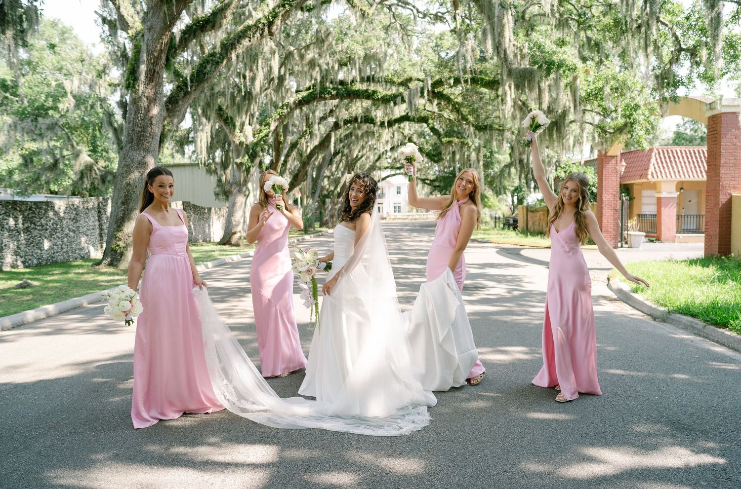 Wedding party in pink bridesmaid dresses posing under Spanish moss-draped trees.