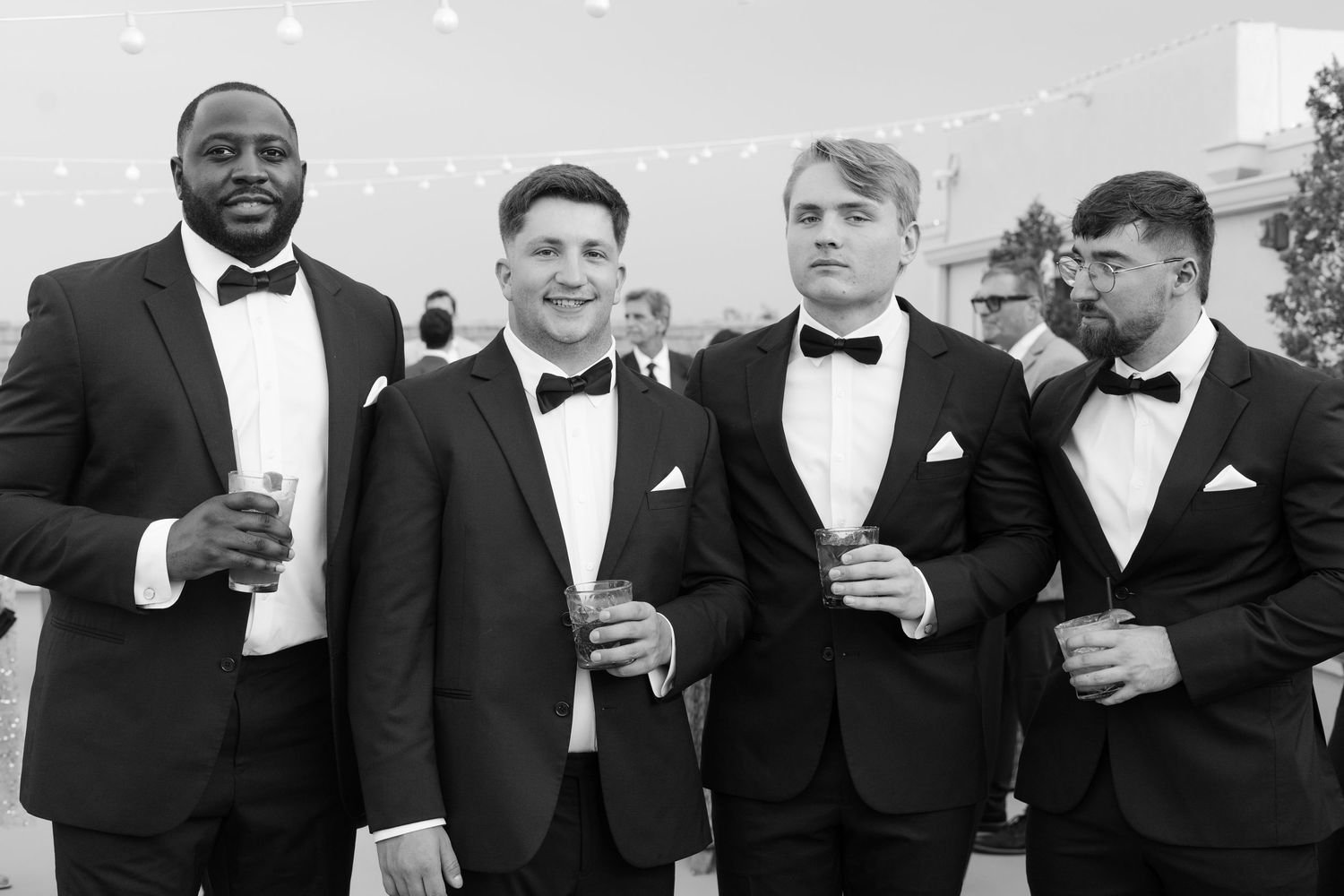 Groomsmen in black tuxedos and bowties pose together at formal event.