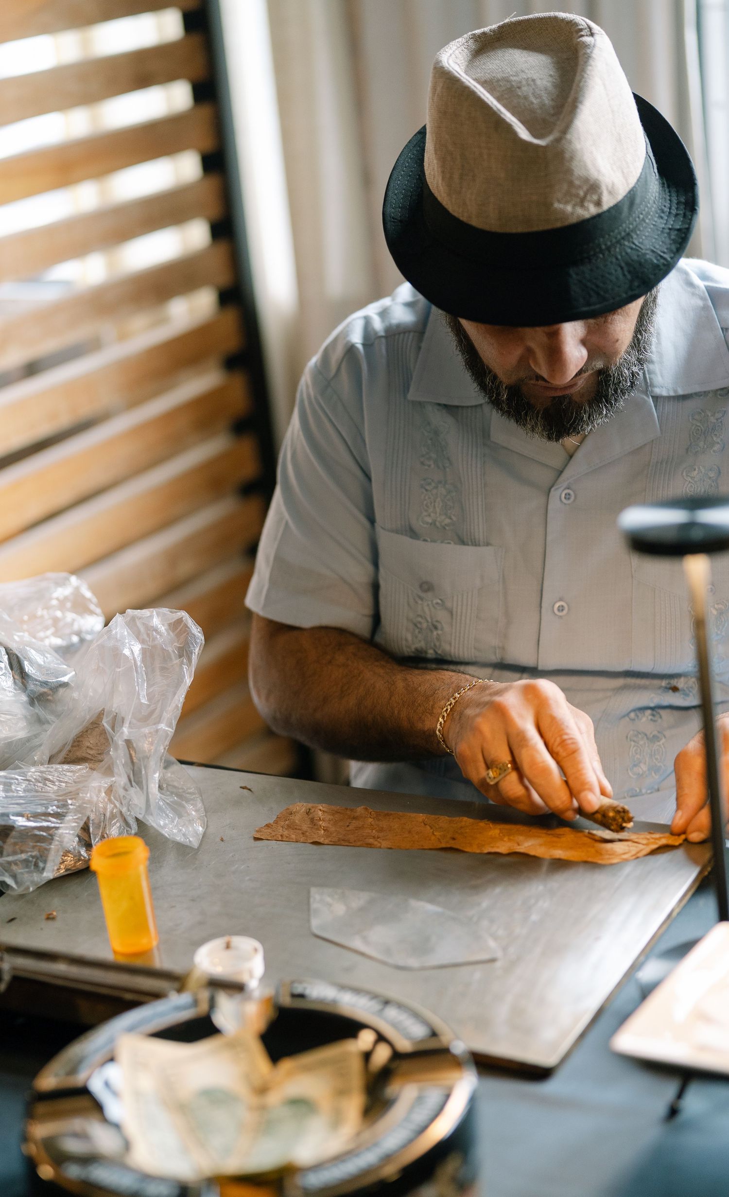Person wearing a fedora hat crafting at a table with leather working tools and materials.