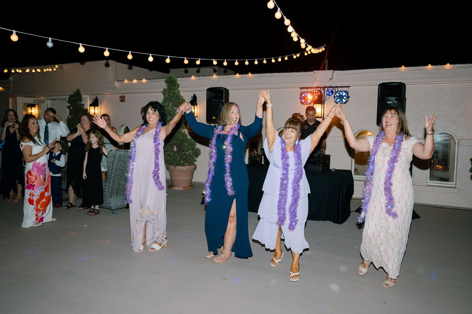 Wedding guests dancing together under string lights at an outdoor reception.