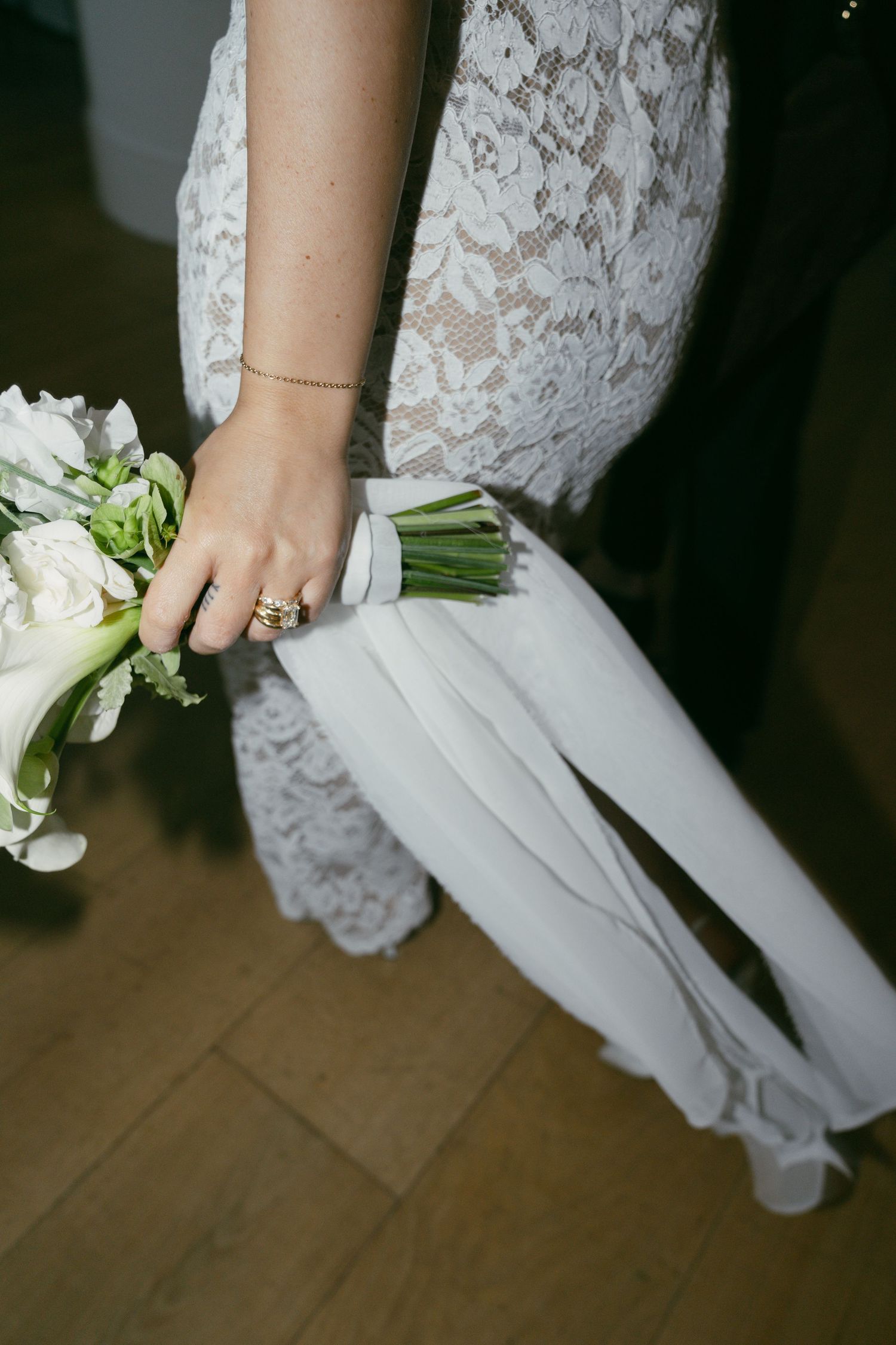 Close-up detail of white lace wedding dress with bridal bouquet and delicate bracelet jewelry.
