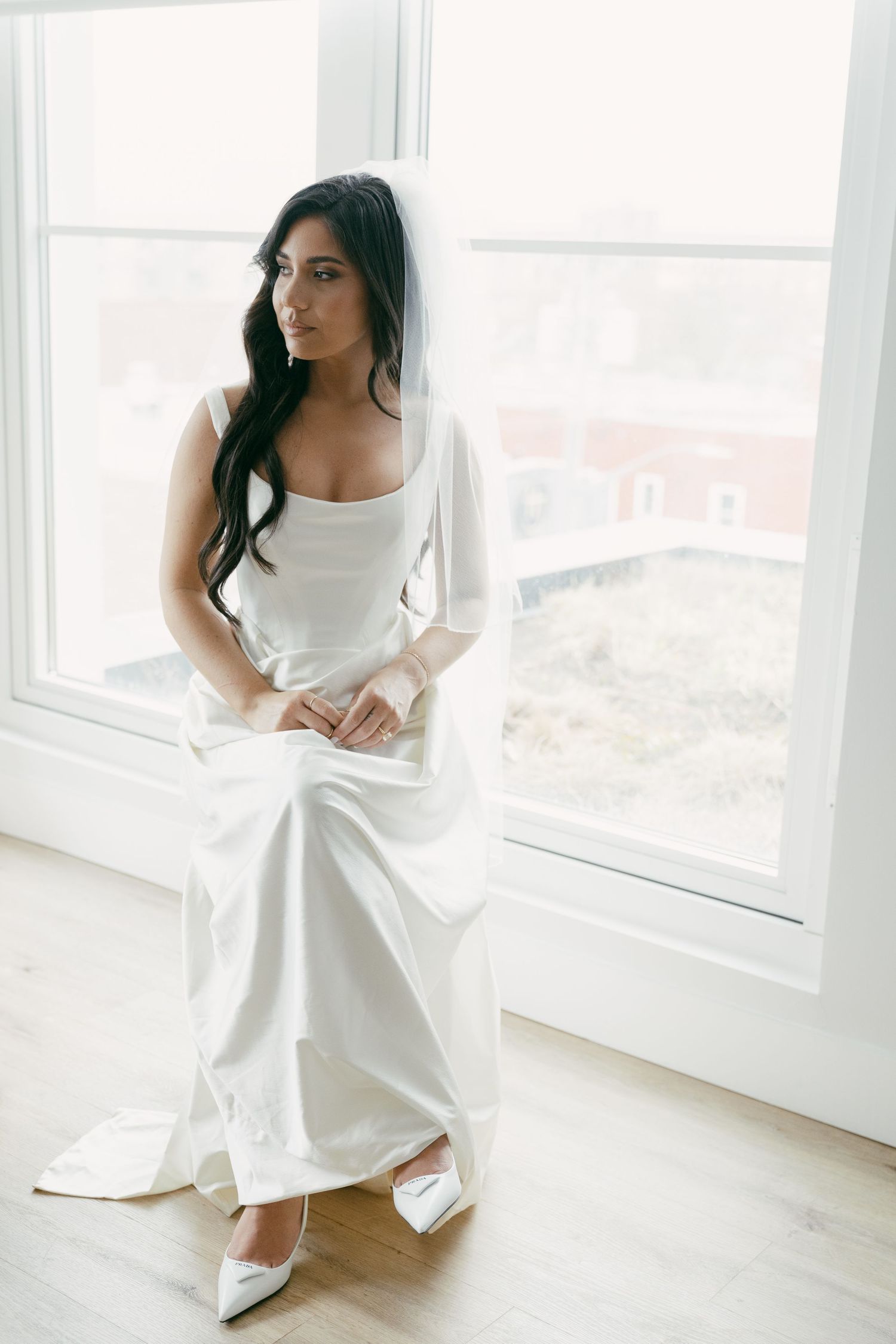 Elegant white wedding dress with long sleeves and square neckline shown near bright window with natural light.