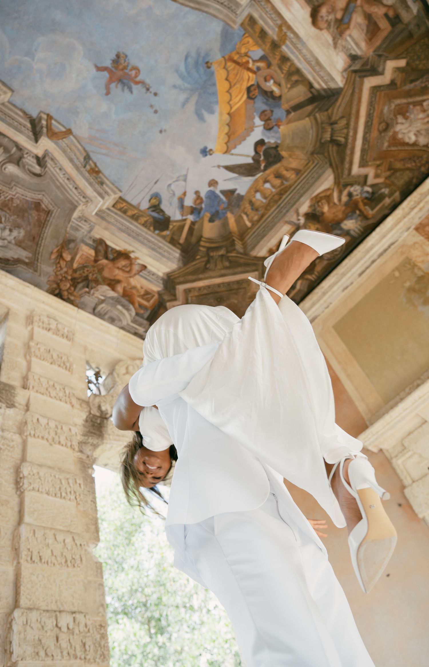 Wedding dress silhouette photographed against ornate baroque ceiling with religious frescoes.