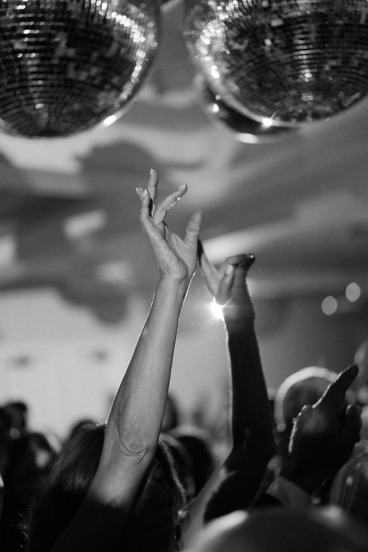 Hands reaching up towards disco balls at a lively dance party with dramatic lighting.