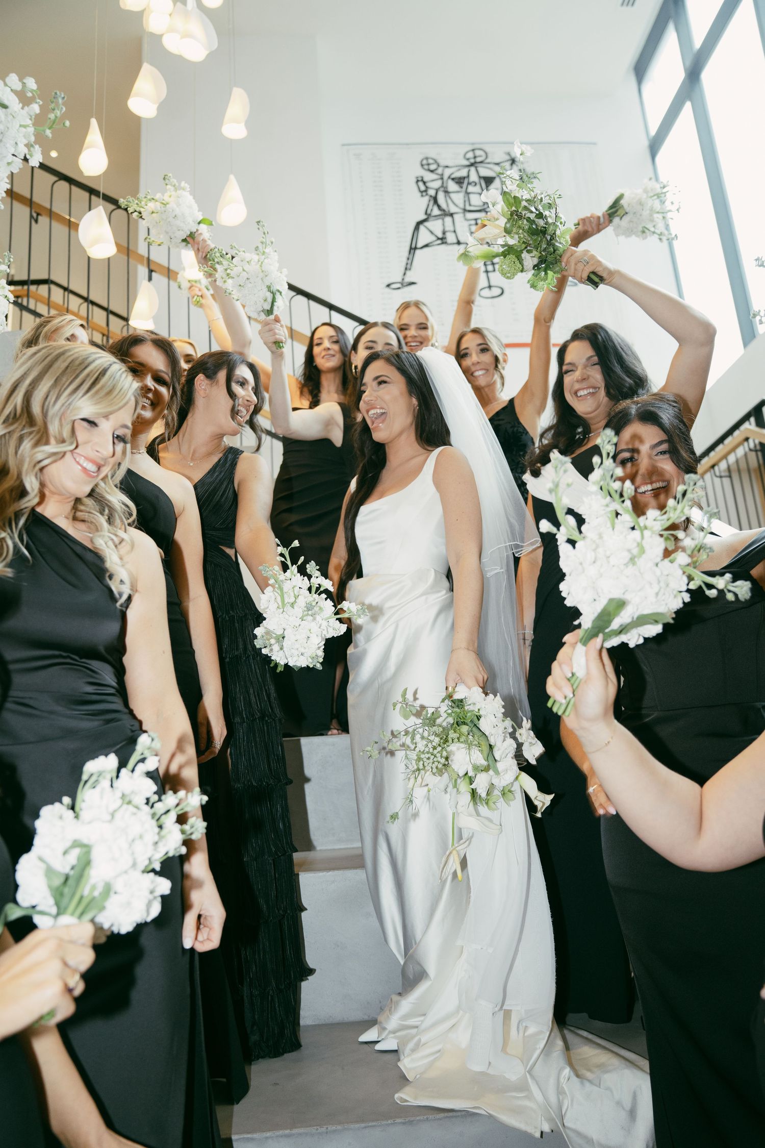 A joyous wedding party celebration on stairs with bridesmaids in black dresses.