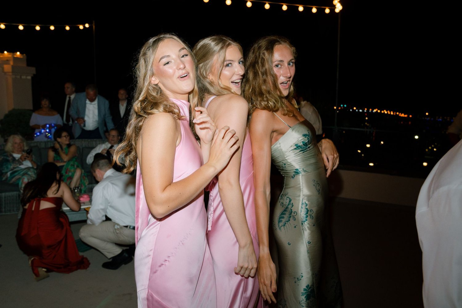 Wedding guests in pink and metallic dresses celebrating at a nighttime reception.