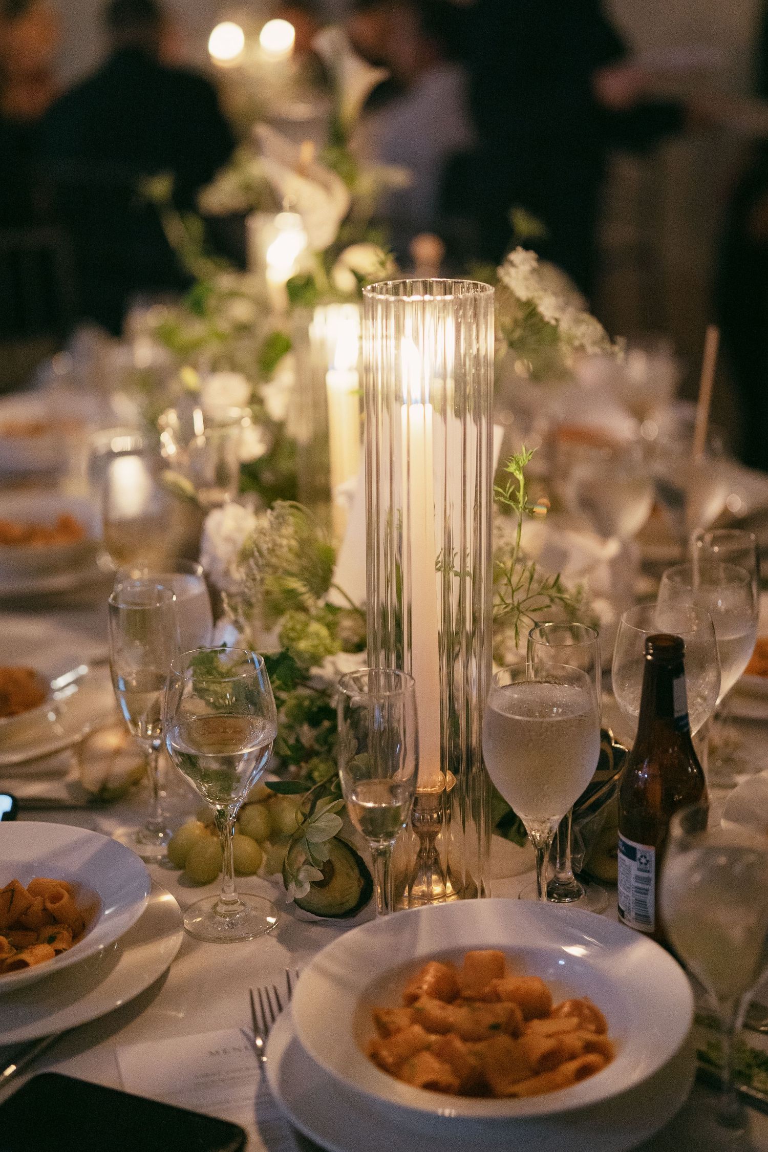 Elegant wedding reception table setting with glowing candle centerpiece, wine glasses and appetizer plates at dusk.