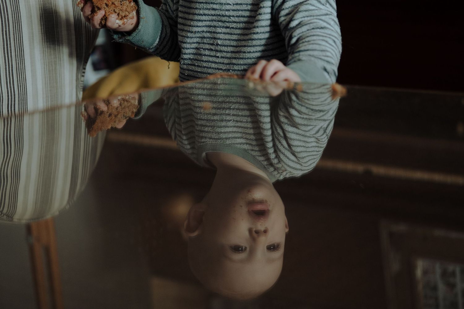 Baby holding a piece of cake with reflection of baby in glass table, captured by Wouter Kleynhans during family shoot at home in Pretoria