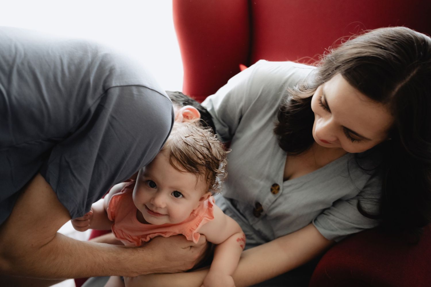 Girl looking at camera while her dad tickles her, and her mom holding her, smiling. Casptured by Wouter Kleynhans during home family shoot