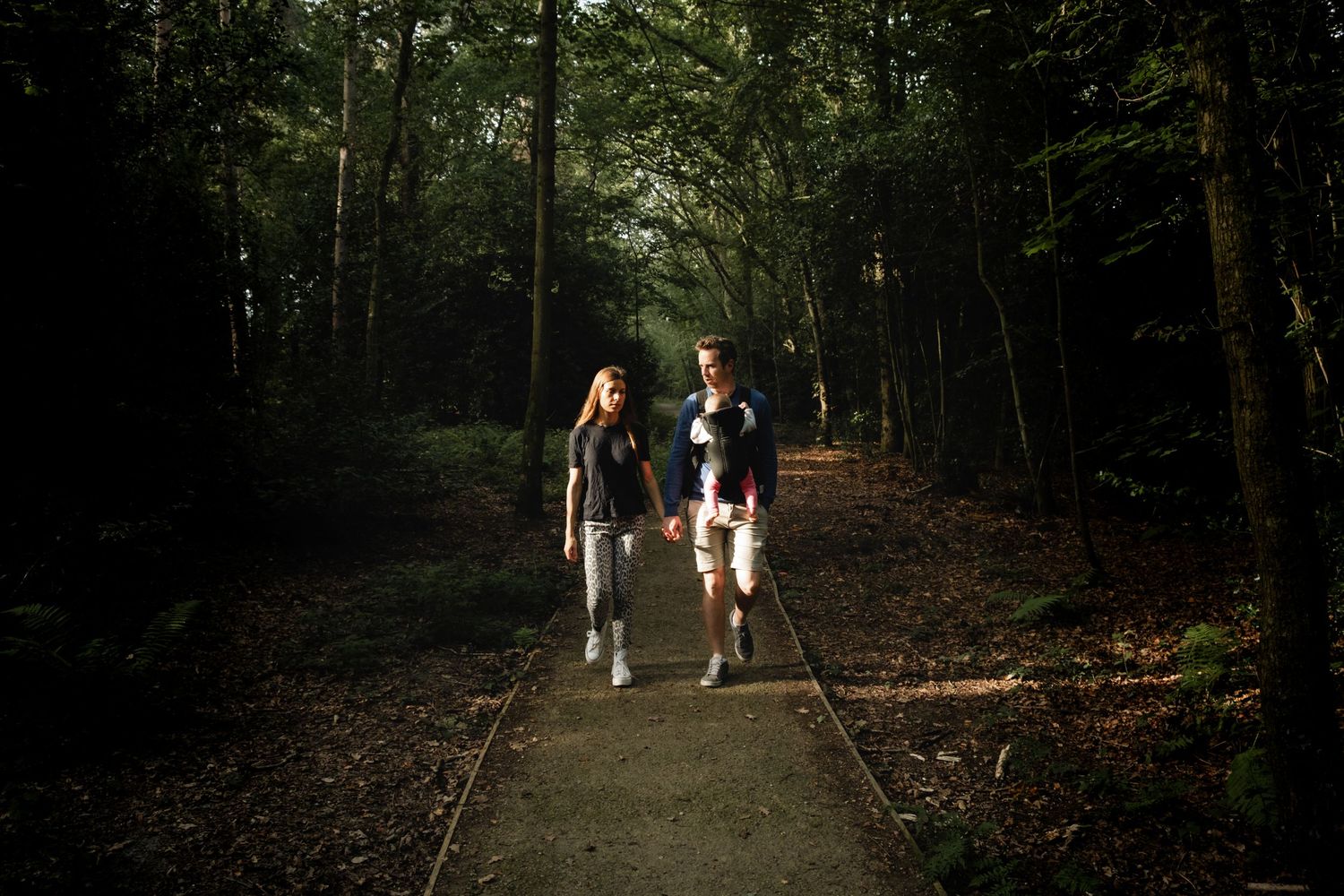 man and women walking while holding hands in forrest near London. Baby in carrier in-front of dad. Captured by Wouter Kleynhans in UK
