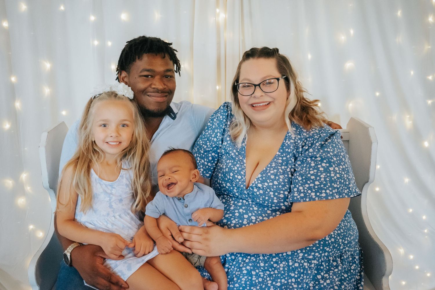Family portrait with baby in front of twinkle light backdrop.