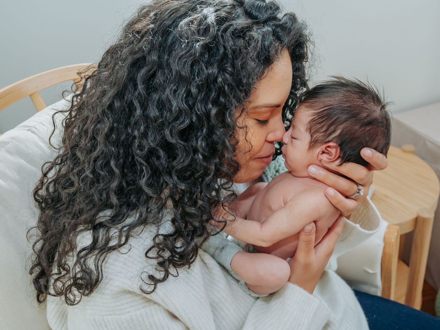 A tender moment is shared between a woman with long curly dark hair and a newborn baby.
