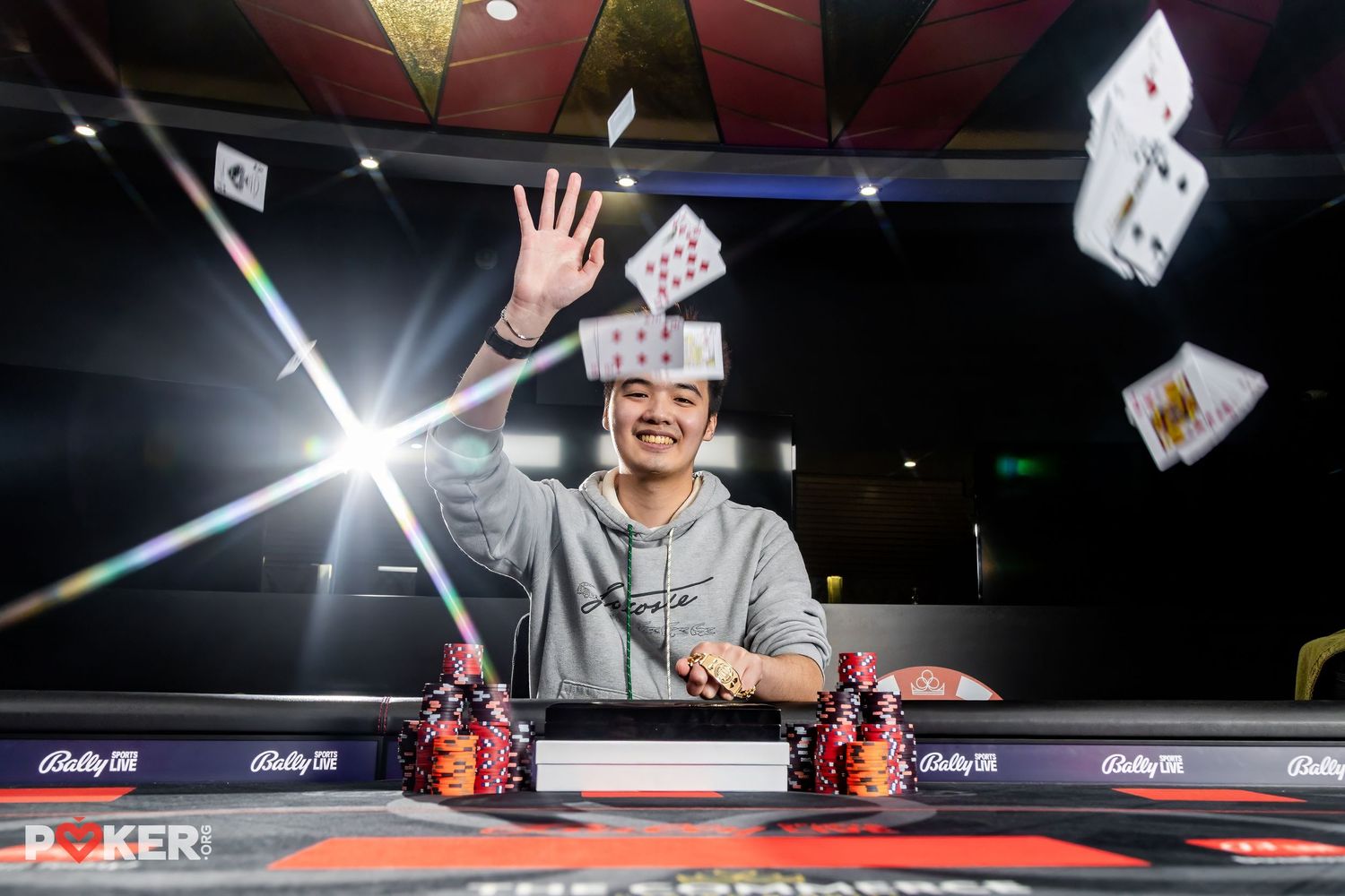 A poker player celebrates at a gaming table as playing cards fly through the air with dramatic lighting effects.