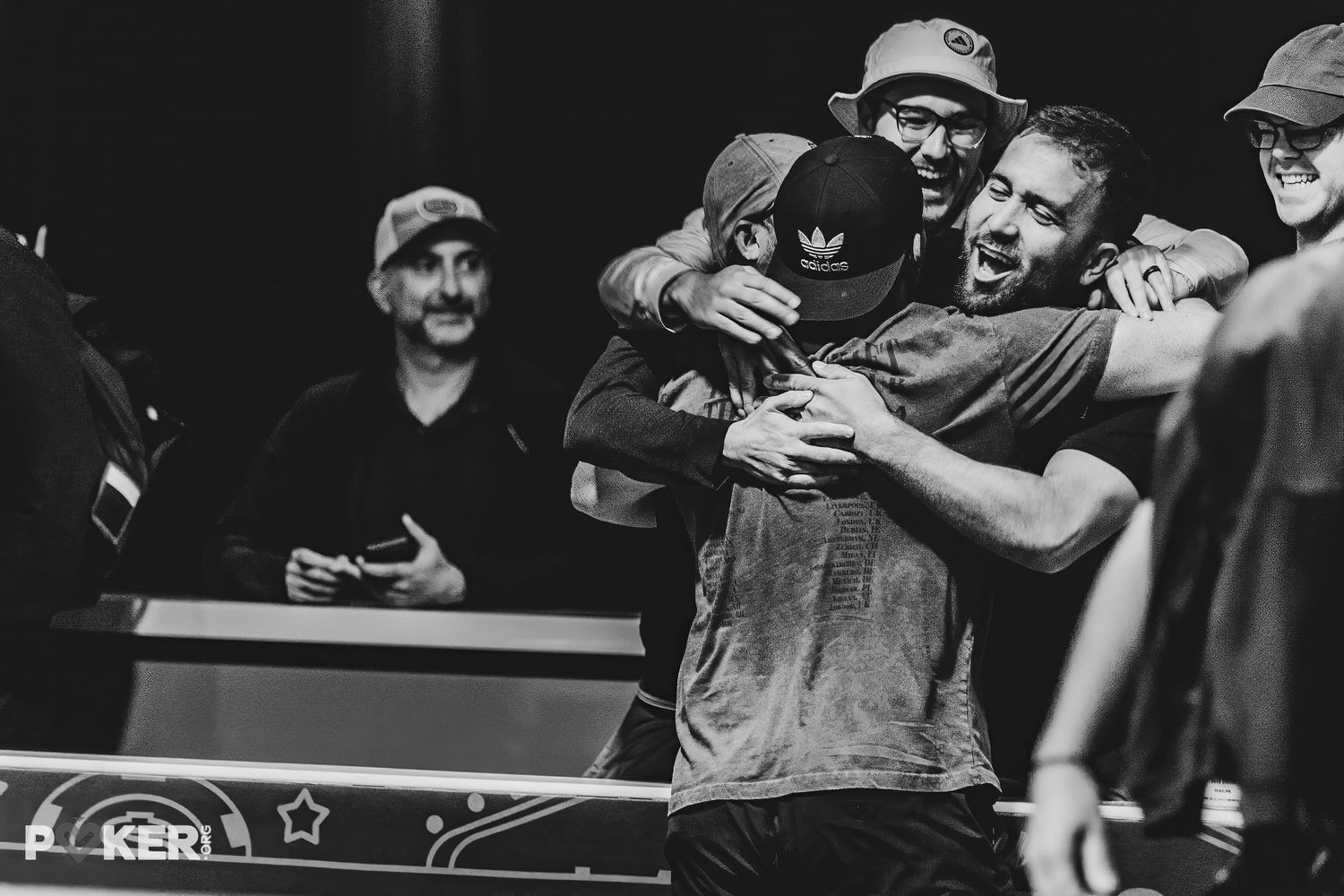 Musicians hugging and embracing in joyful celebration backstage at a concert venue, captured in black and white.
