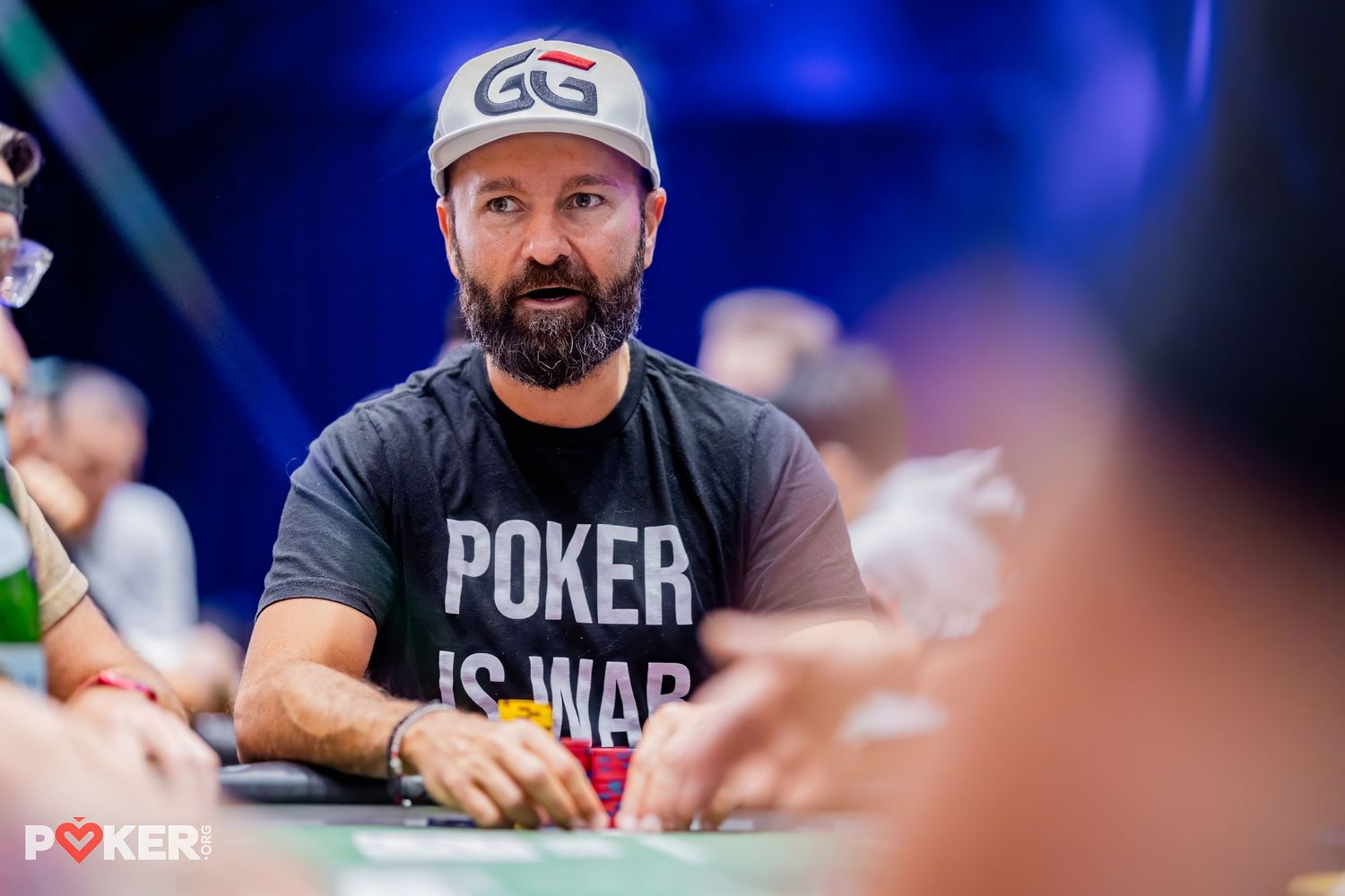Professional poker players compete at a high-stakes tournament table with blue lighting and casino atmosphere.