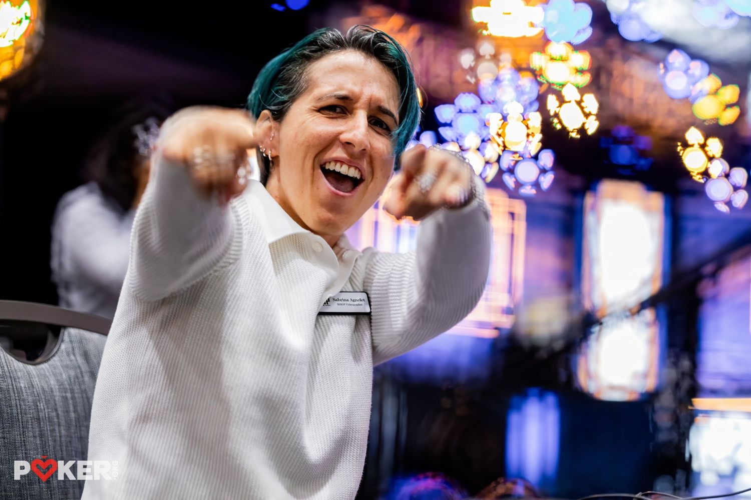 A person reacts emotionally with raised arms against blurred purple and blue lights at a World Series of Poker event.