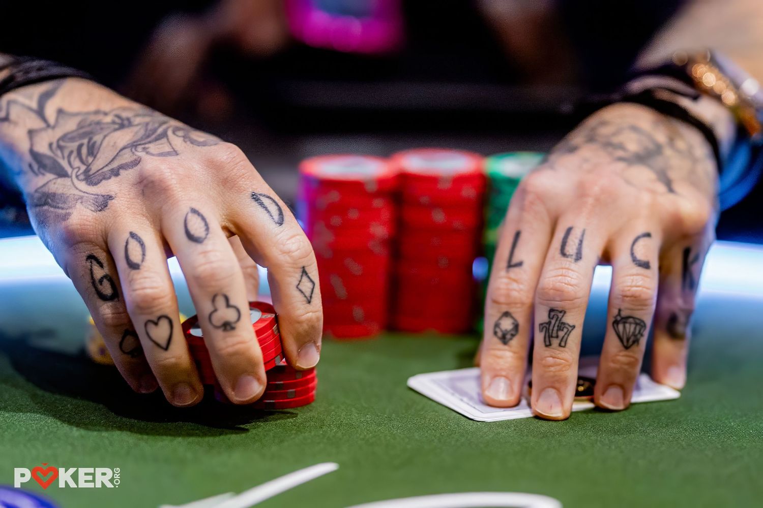 Close-up view of tattooed hands shuffling poker chips at a casino gaming table during play.