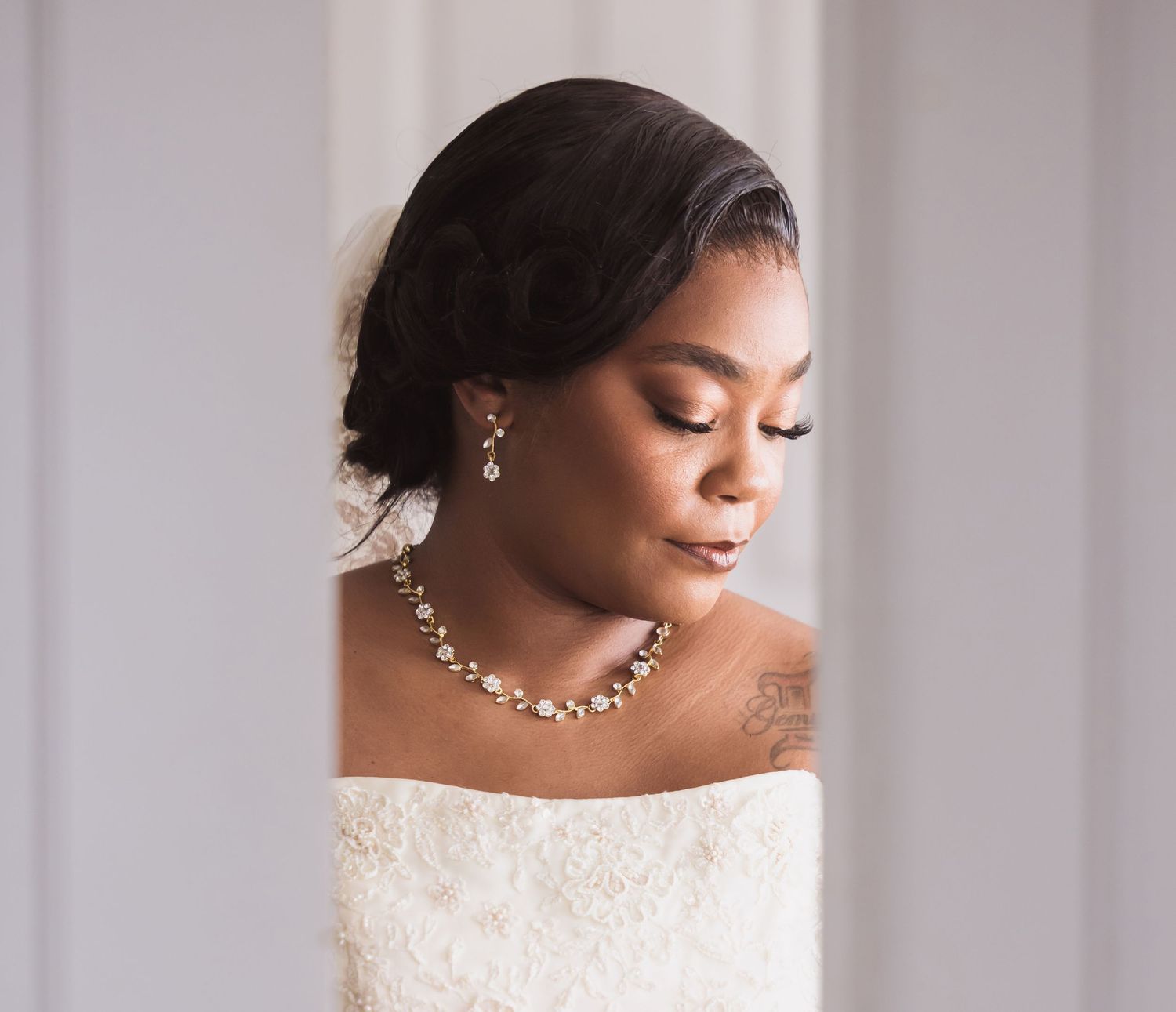 Elegant bride wearing off-shoulder wedding gown with delicate jewelry and natural makeup.