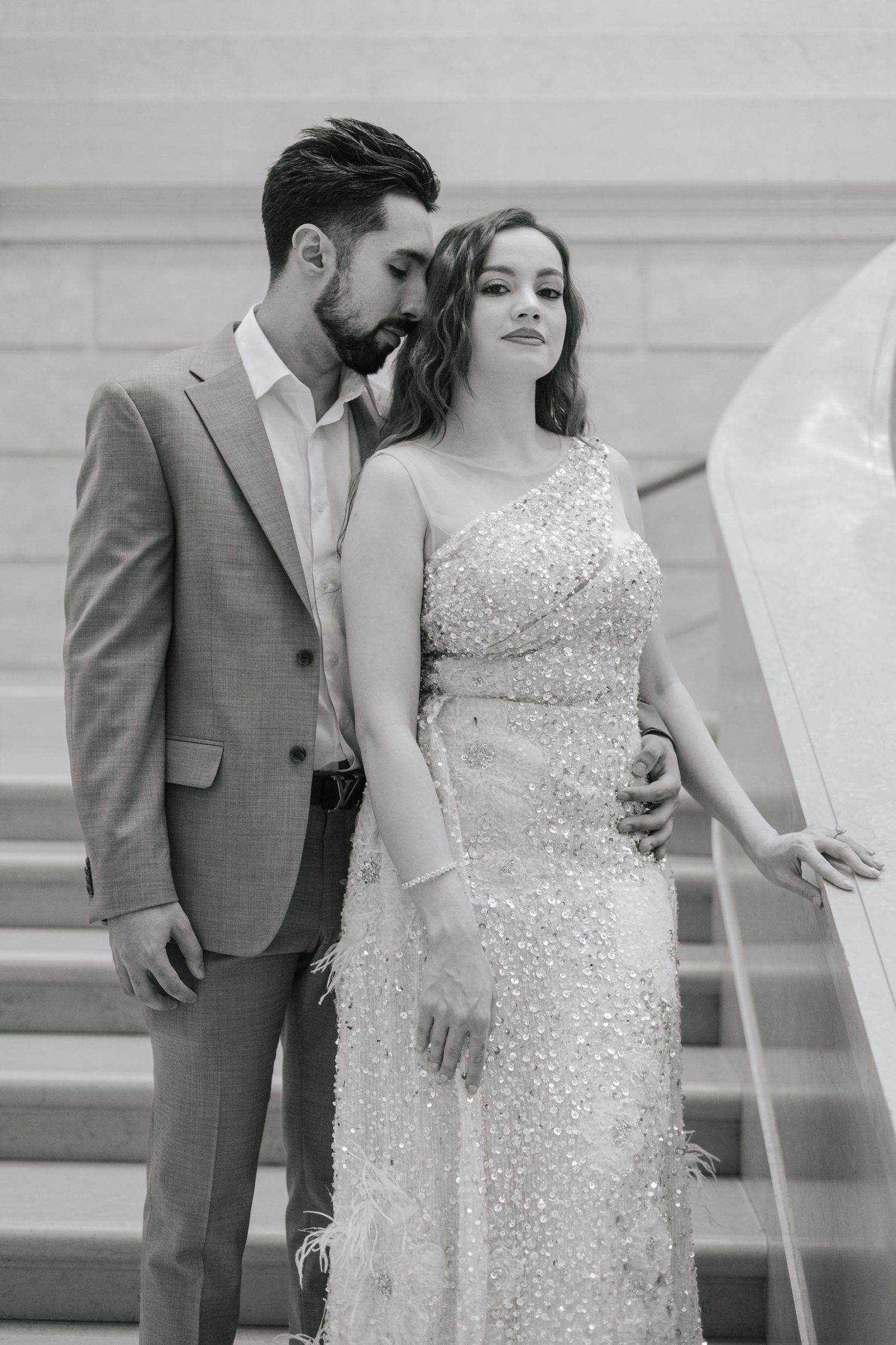 A romantic black and white photo of a couple in formal attire standing on stairs.