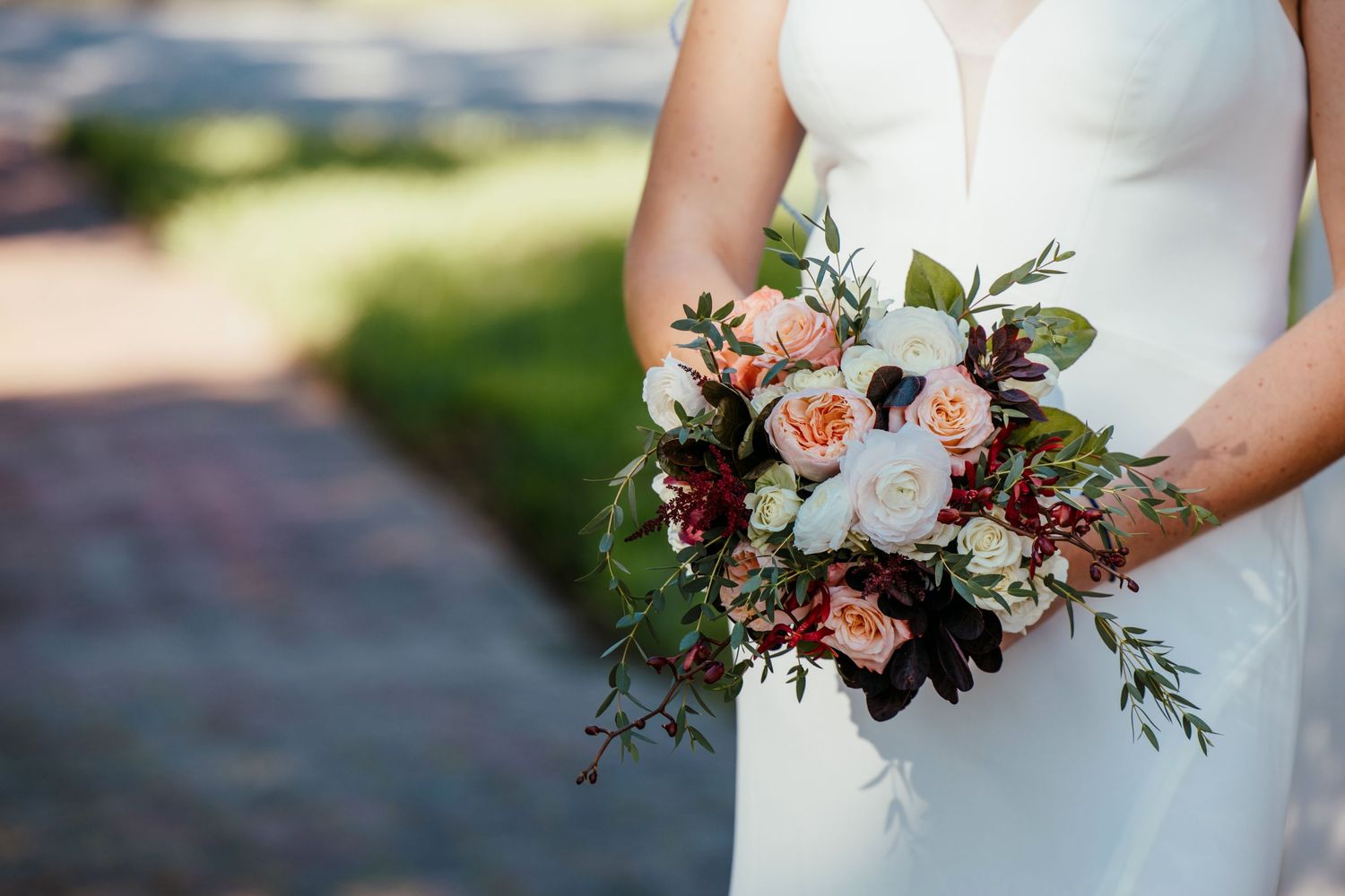 Close-up of bridal bouquet with peach roses and white flowers against white wedding dress.