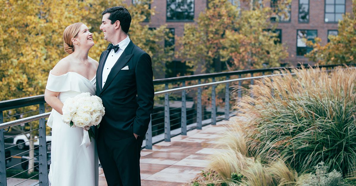 Newlyweds sharing an intimate moment on a terrace with autumn foliage in background.