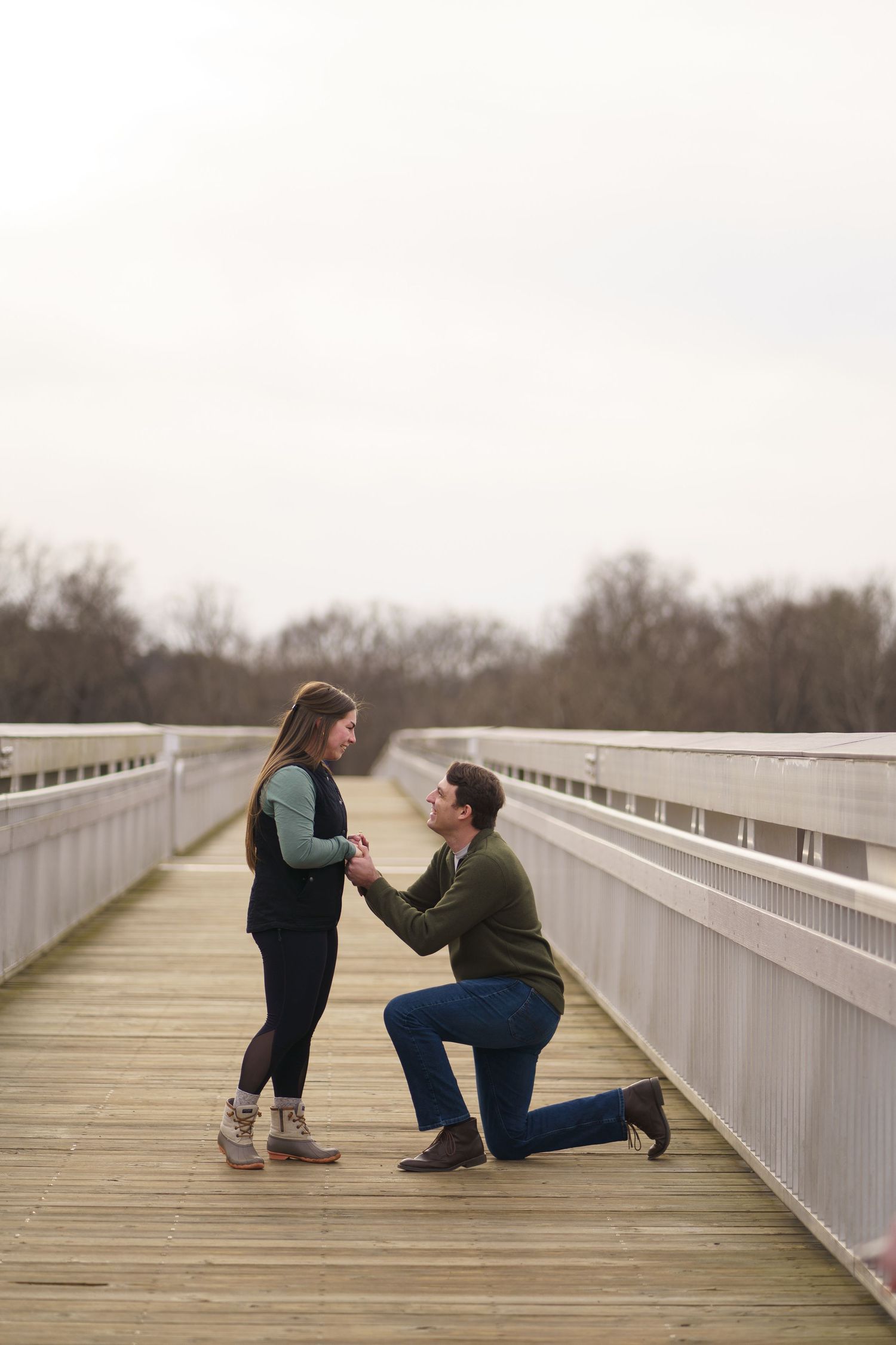 Romantic proposal moment captured on wooden bridge during sunset.