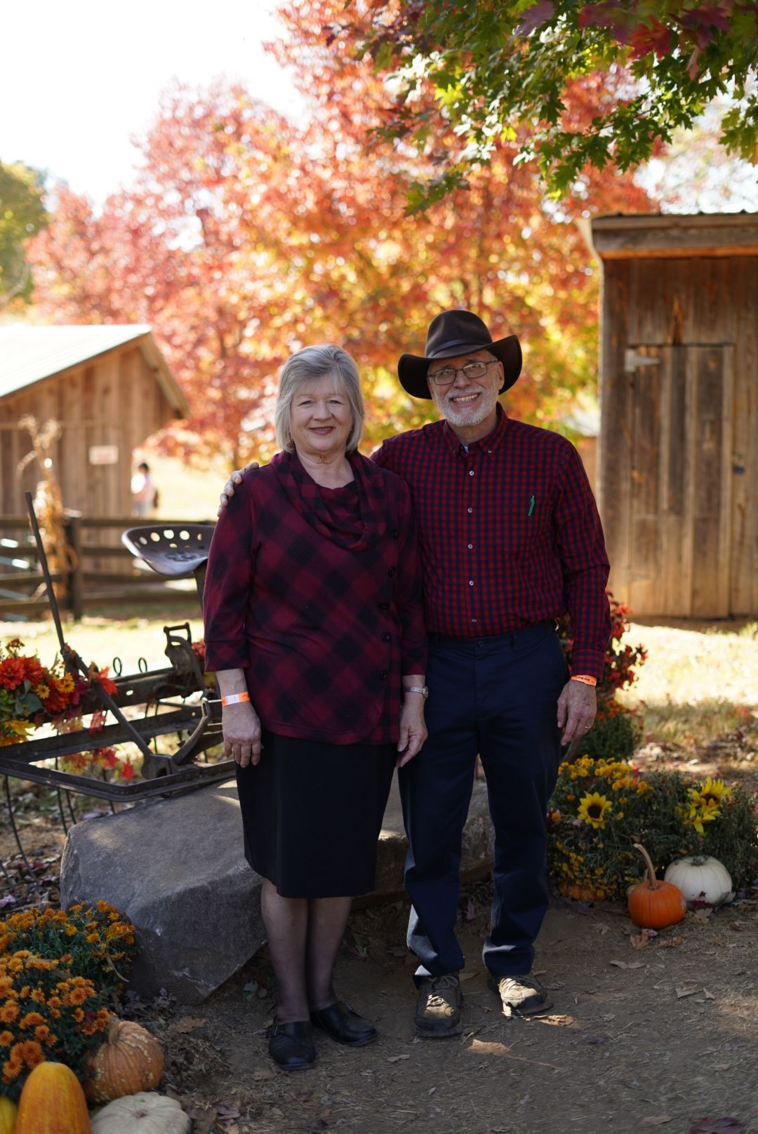 Couple in matching plaid outfits posing by rustic cabin with fall decorations.