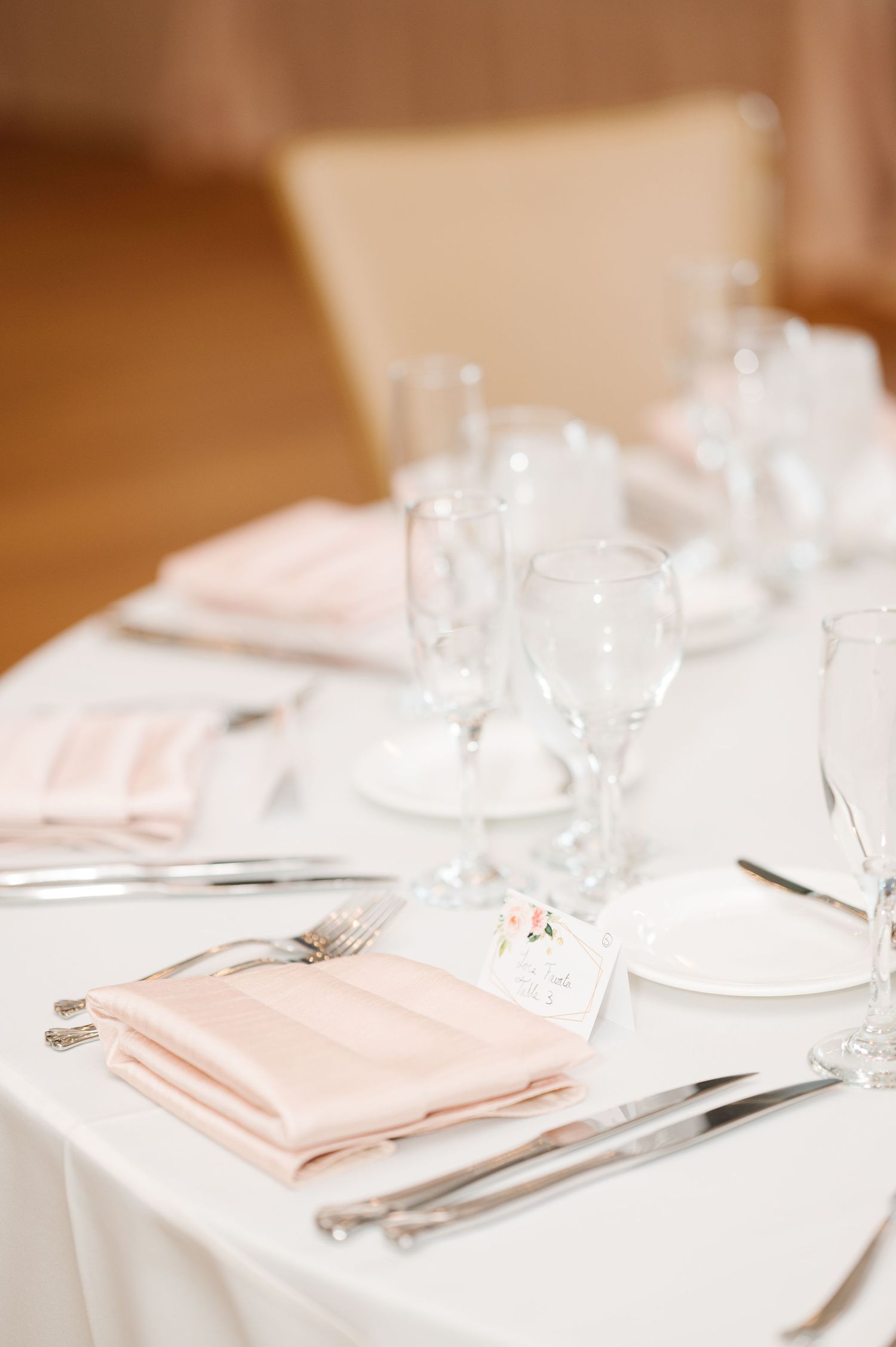 Elegant table setting with soft pink napkins, white tablecloth, and crystal glassware for a formal dining experience.